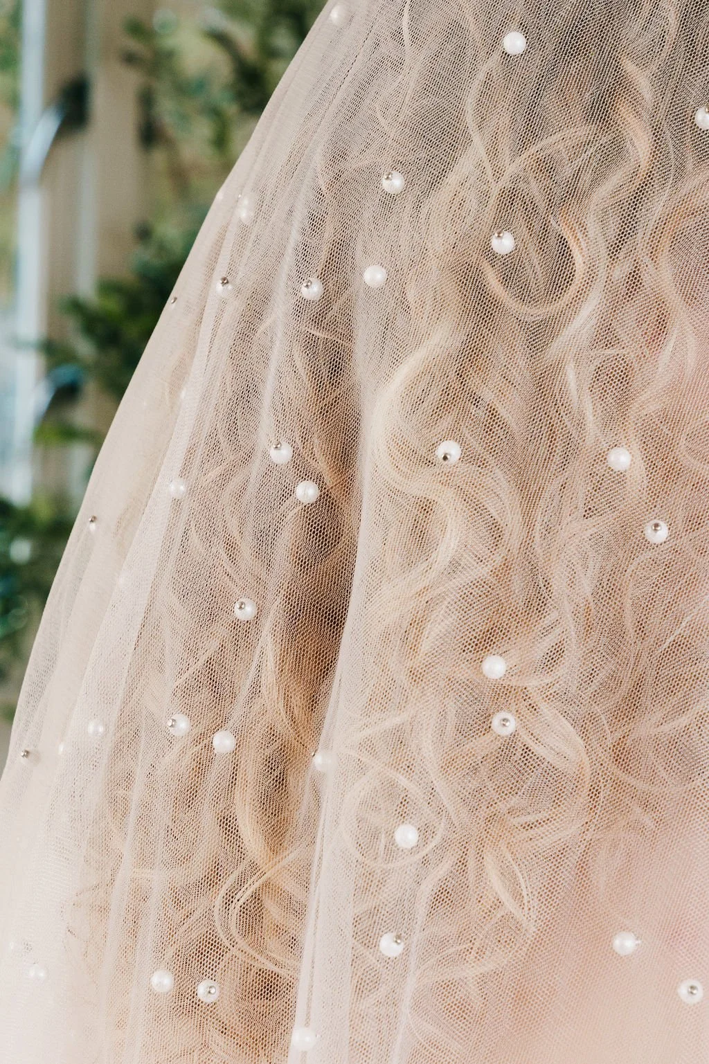 Close-up of a delicate, light-colored fabric decorated with small pearl beads and intricate embroidery, likely part of a wedding dress or formal gown.