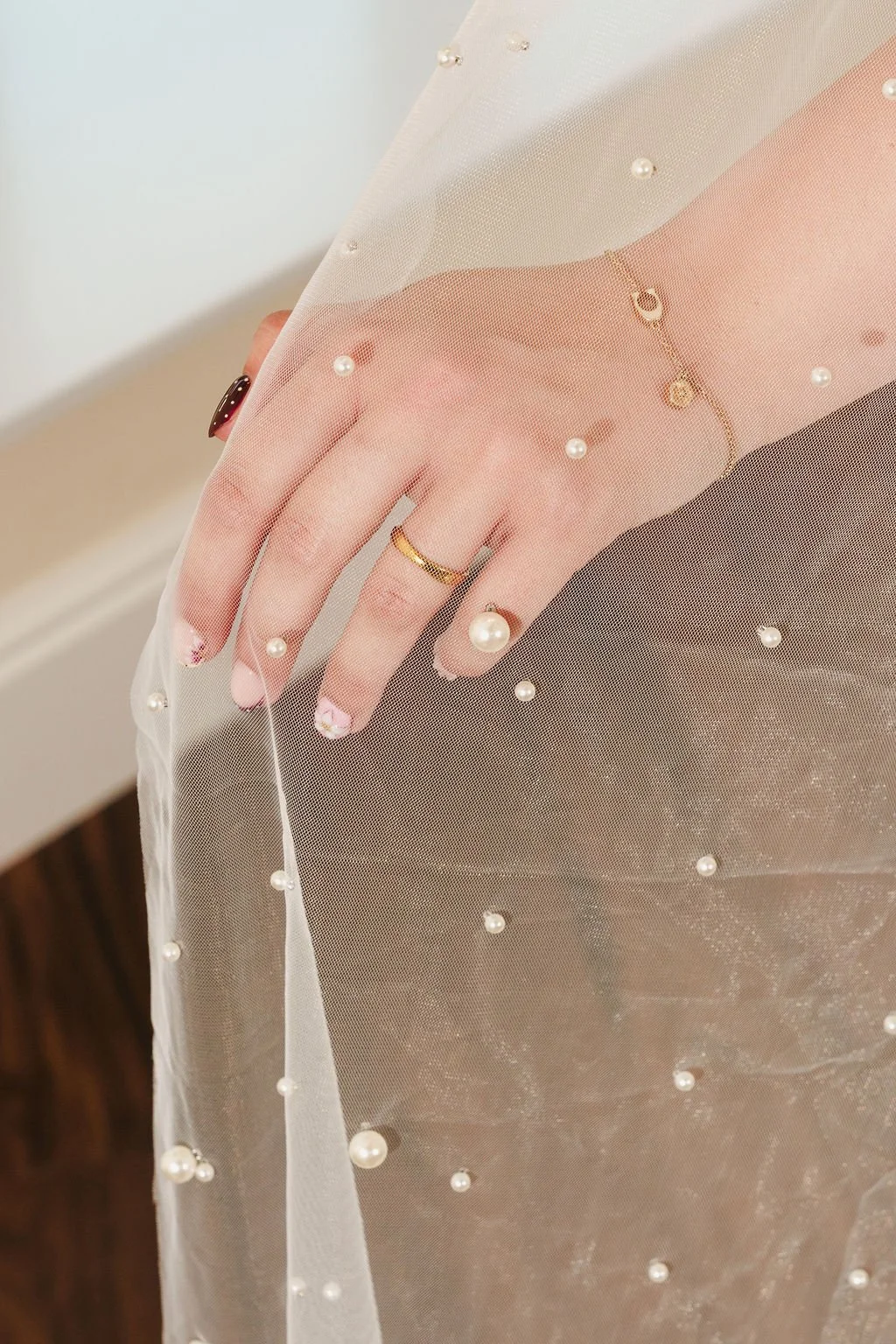 A close-up of a hand with rings, wearing a sheer, pearl-embellished fabric covering the hand and wrist.