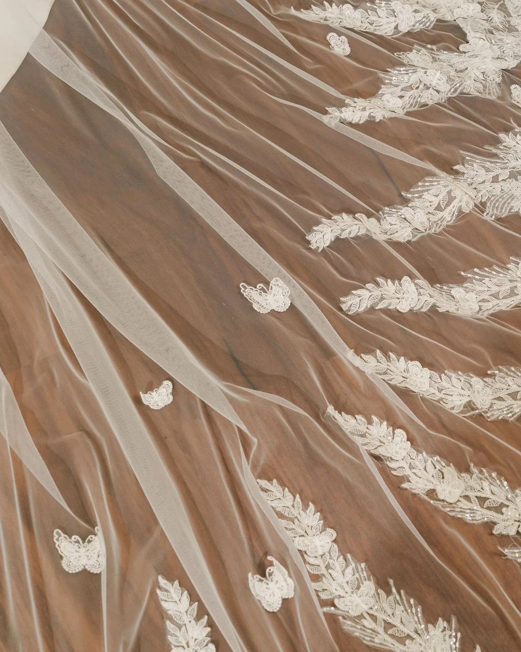 Close-up of sheer fabric with white floral embroidery and butterfly appliques, draped and flowing.