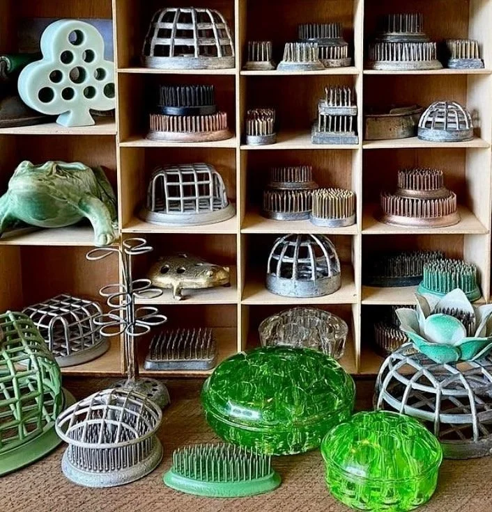 Collection of vintage metal and glass flower frogs displayed in wooden cubbies