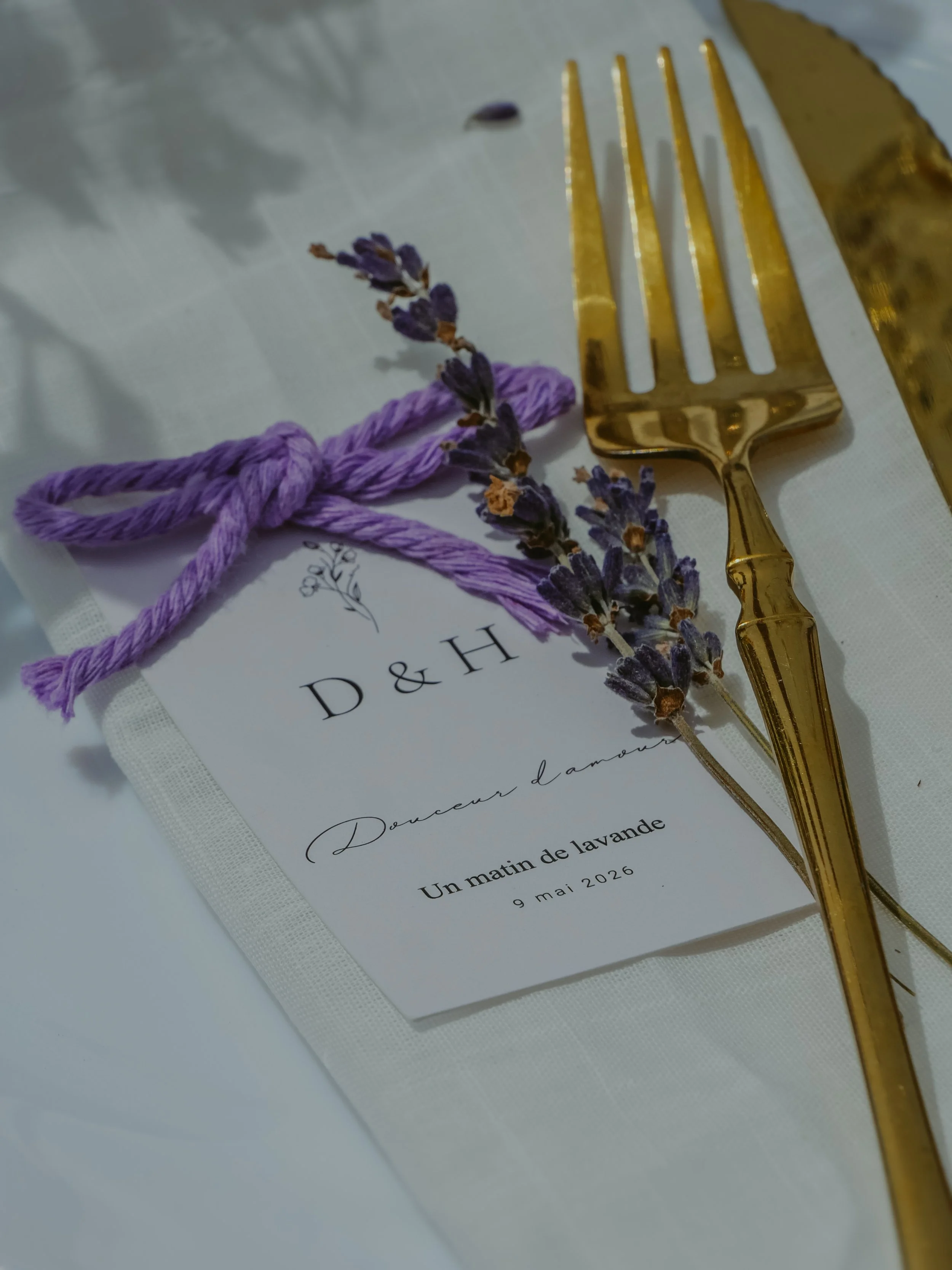 Une nappe blanche avec un menu, une branche de lavande, un ruban violet et une fourchette dorée.