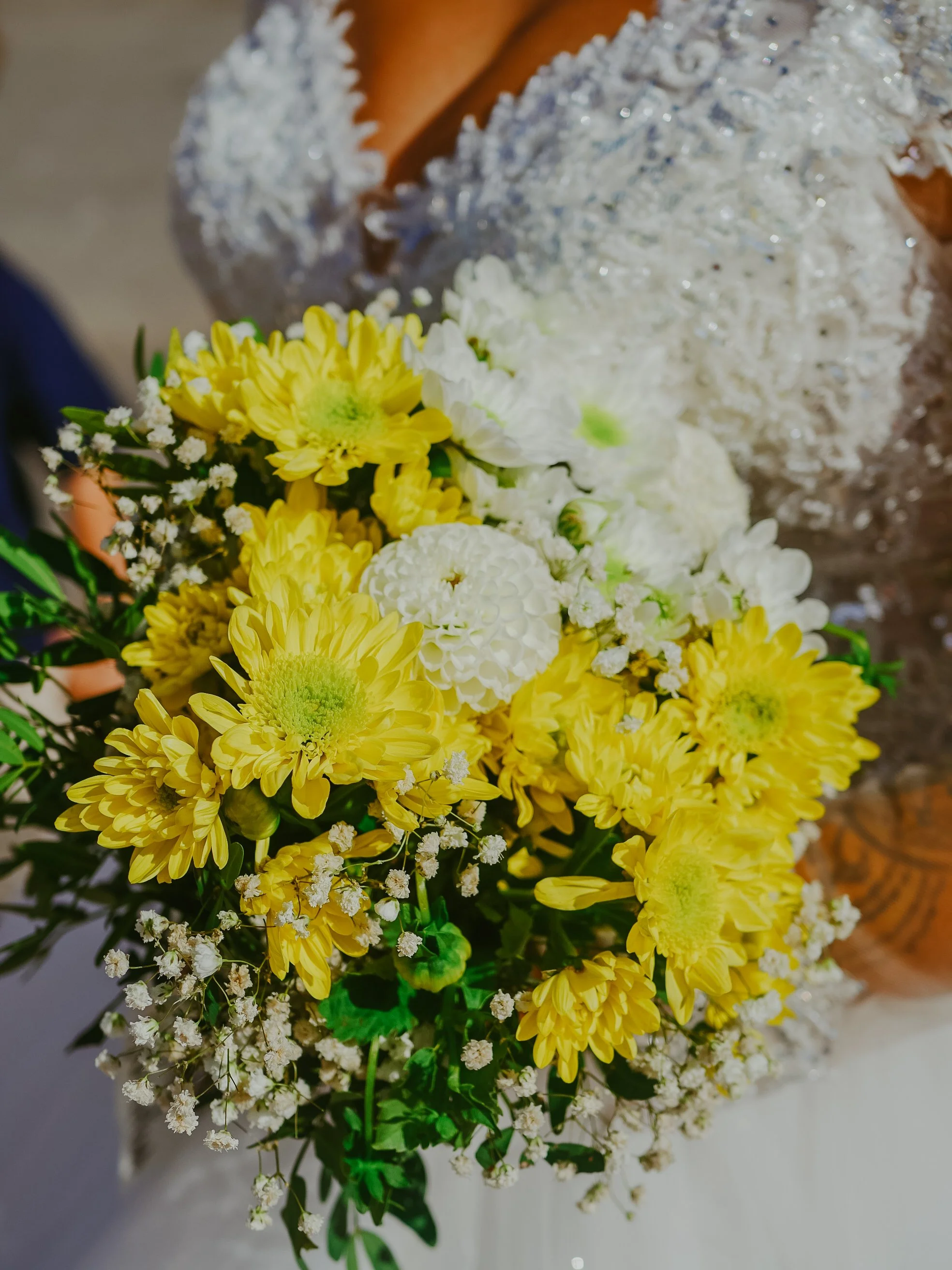 Bouquet de fleurs composé principalement de chrysanthèmes jaunes et de petites fleurs blanches.