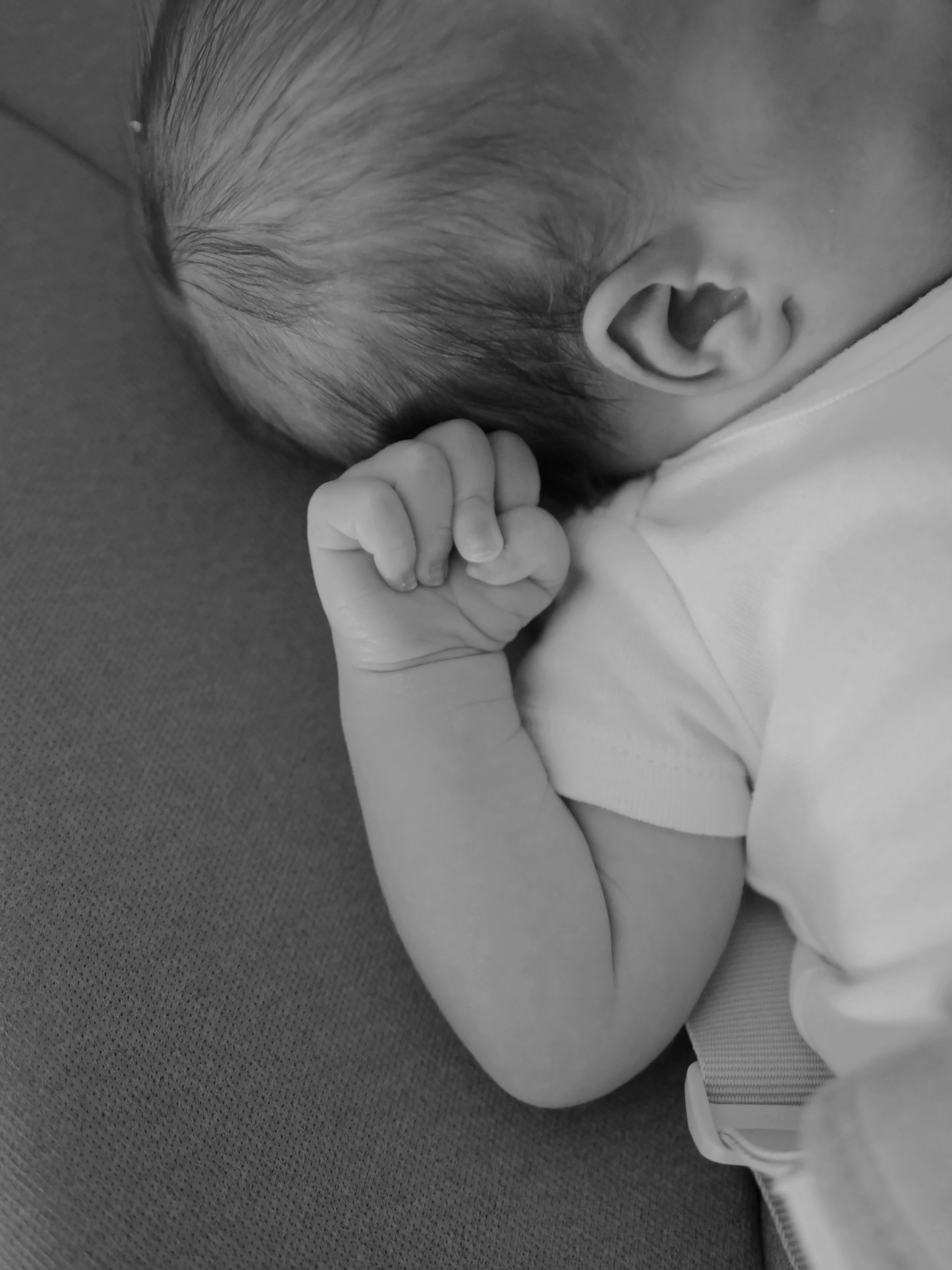Un bébé qui dort, vu de côté, avec la main proche de la bouche, en noir et blanc.