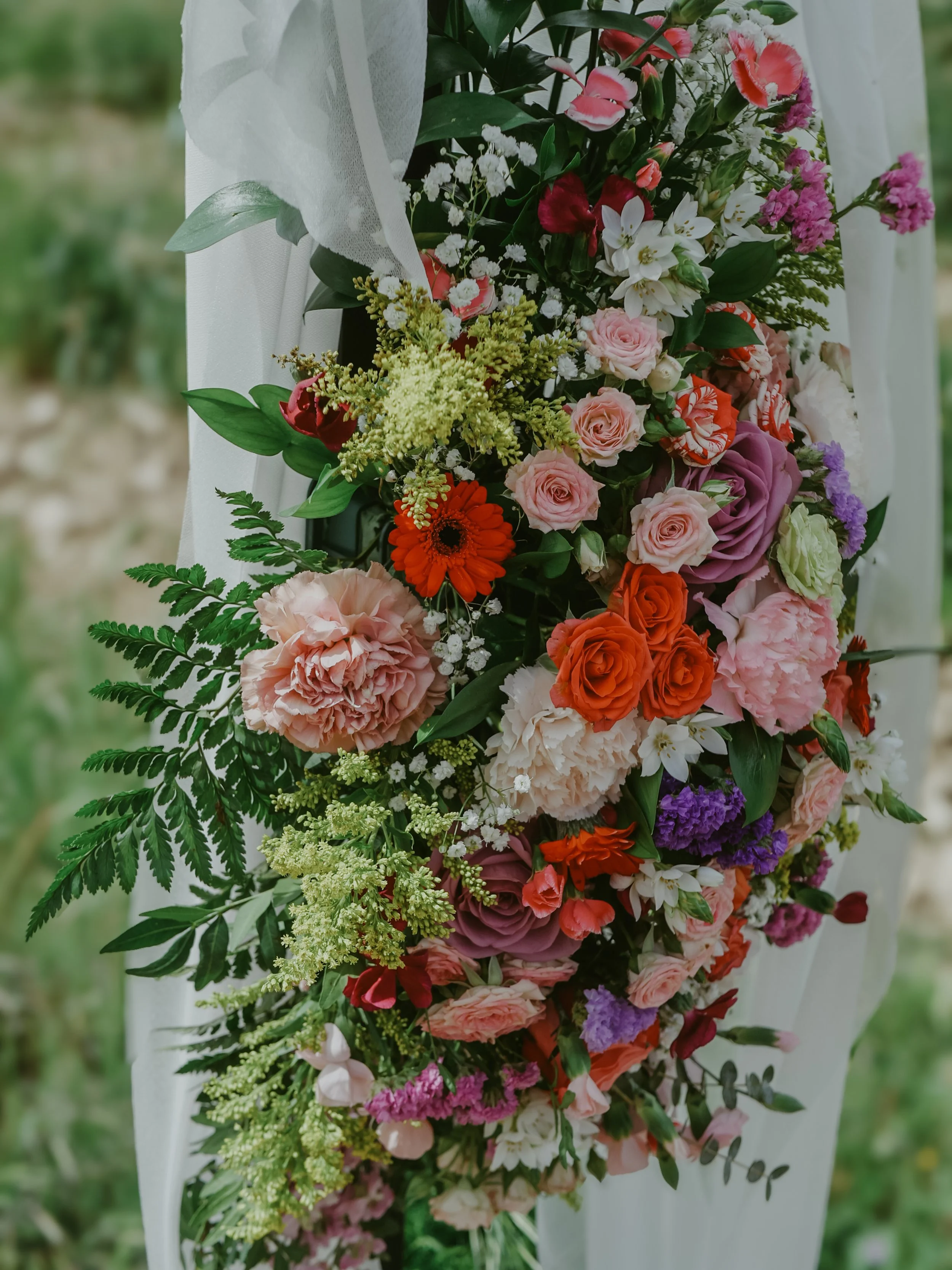 Un bouquet de fleurs colorées avec des roses, des gerberas, et d'autres fleurs, agrémenté de feuillage vert, posé sur une surface blanche likely lors d'une cérémonie ou d'un événement