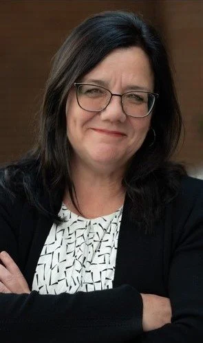 Jenny Svetec, Real Estate Agent, a middle-aged woman with shoulder-length dark hair and glasses, smiling with her arms crossed, wearing a black blazer over a patterned blouse.