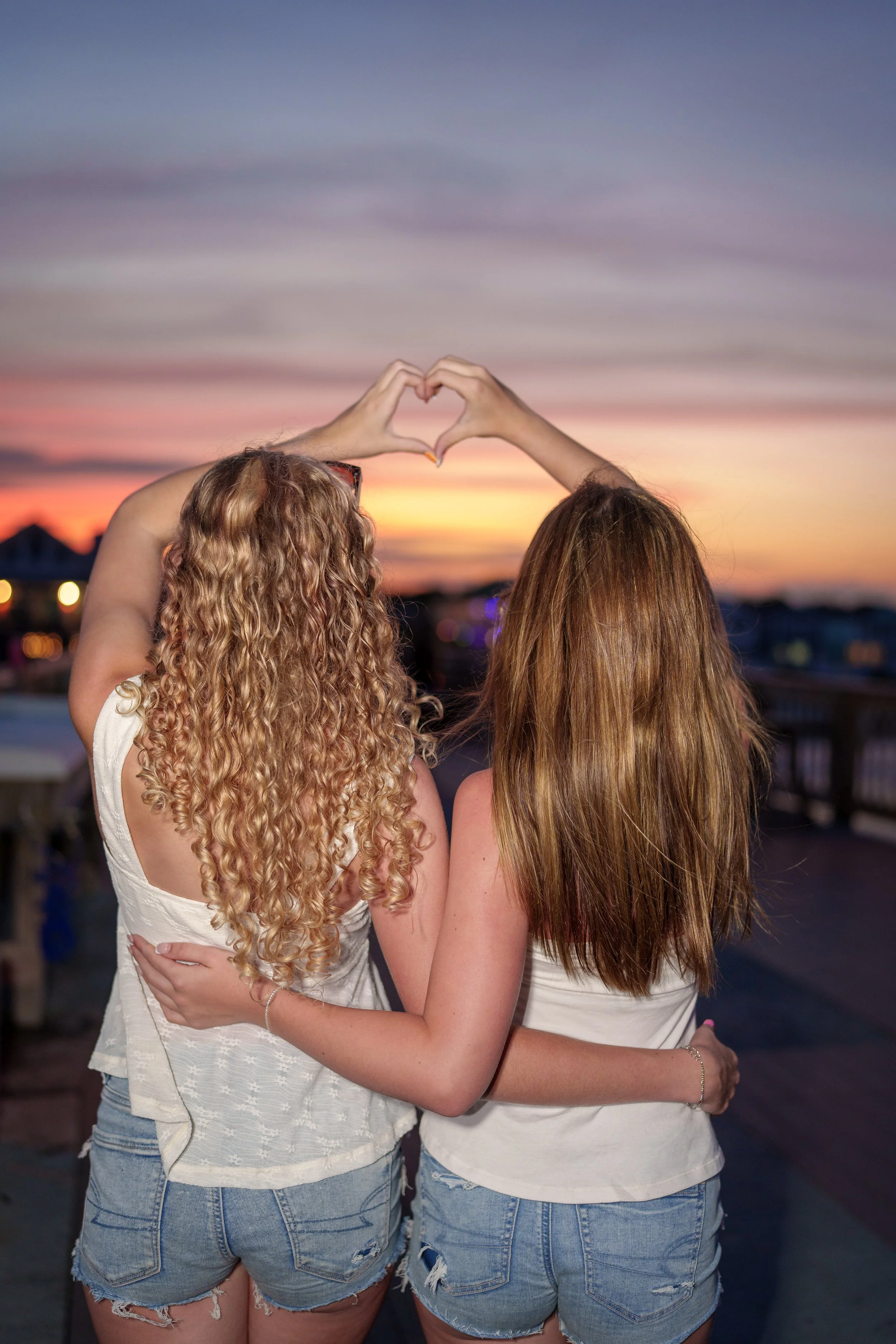 Two people making a heart with their hands against a sunset sky, couples photographer Charlotte area