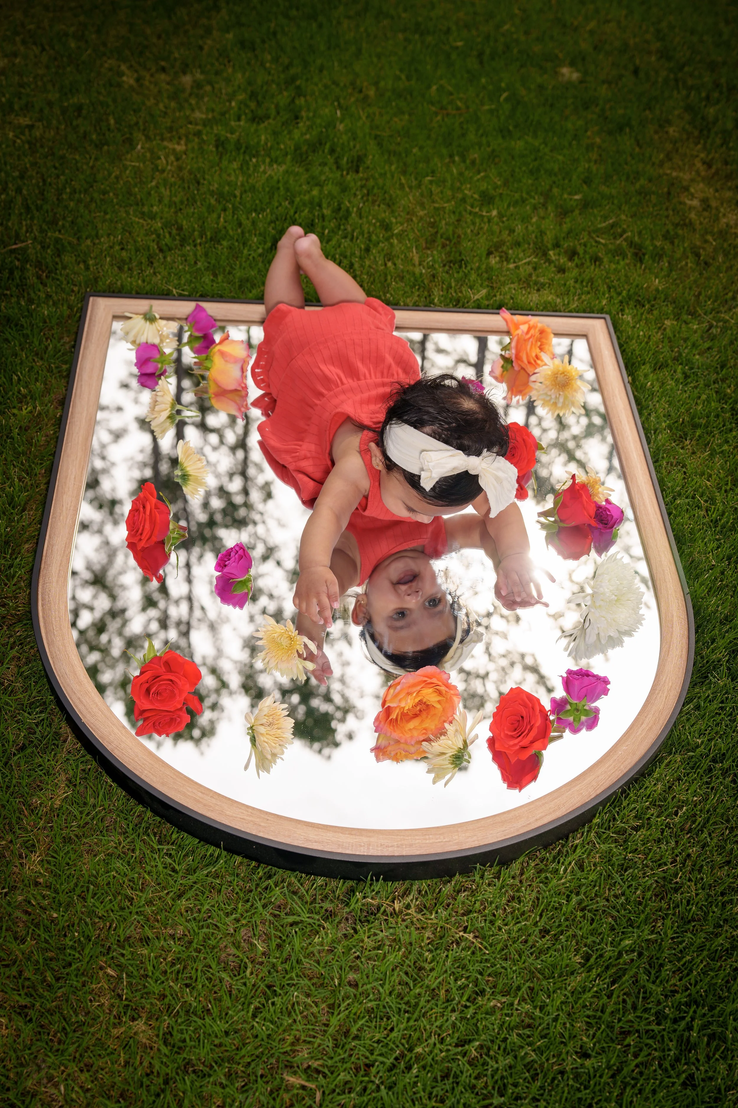 Baby lying on a flower-edged mirror seen from above, milestone photography session Charlotte area