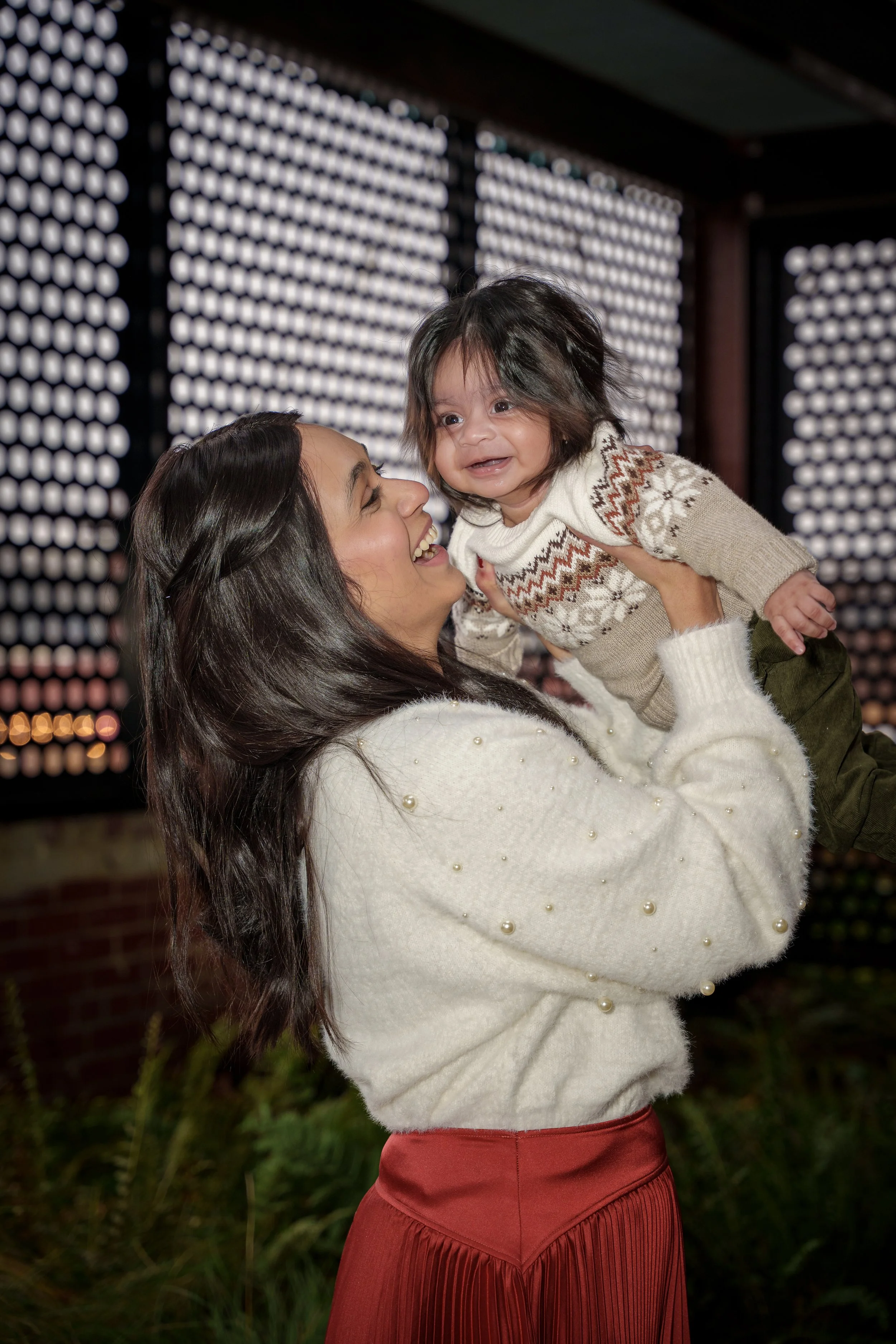 Mother lifting her laughing baby overhead under string lights, family photographer Charlotte NC