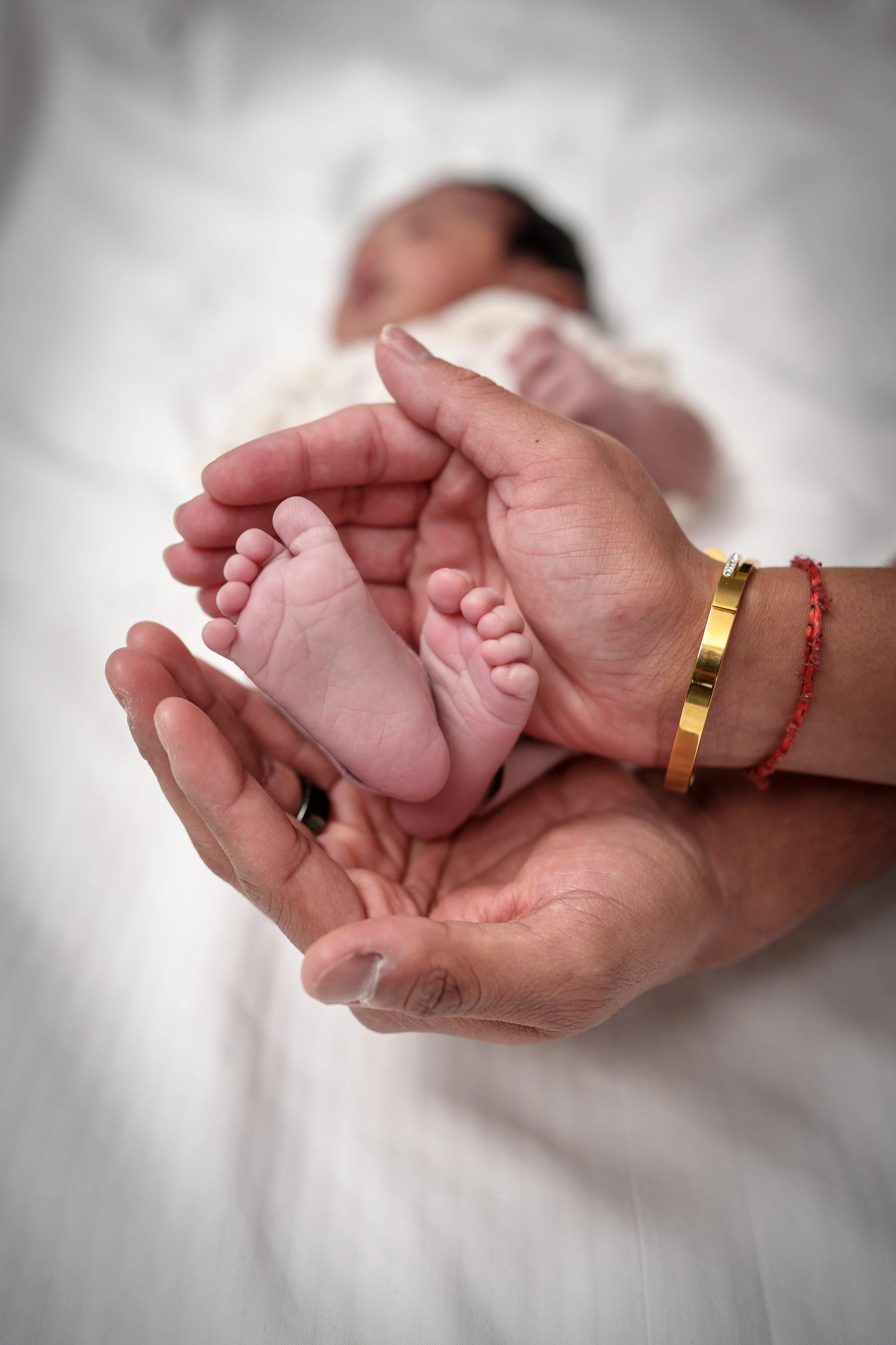 Newborn's feet cradled in parents' cupped hands with gold bangle, newborn photography Fort Mill SC
