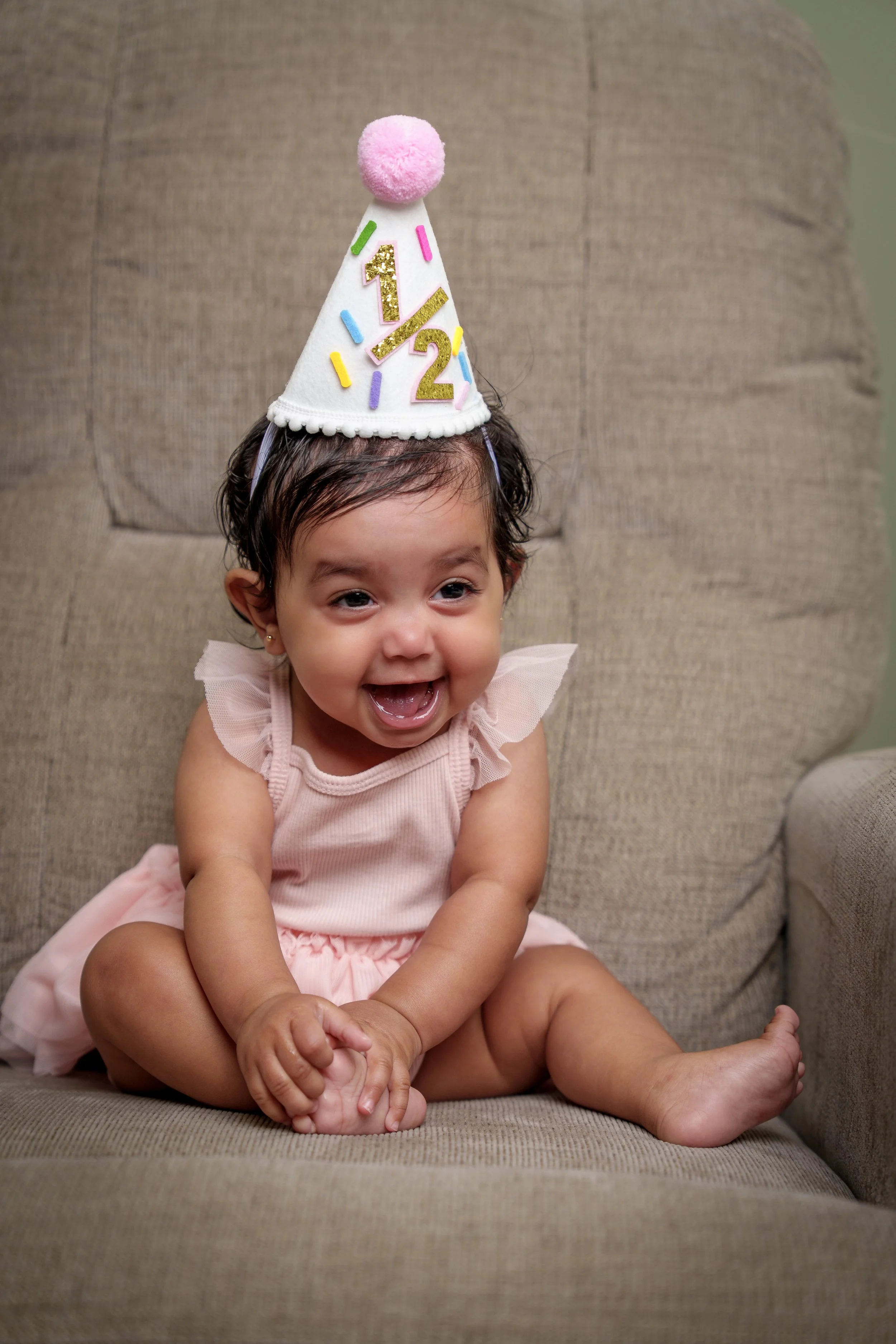 Baby in a half-birthday party hat grinning on an armchair, milestone photography Fort Mill SC
