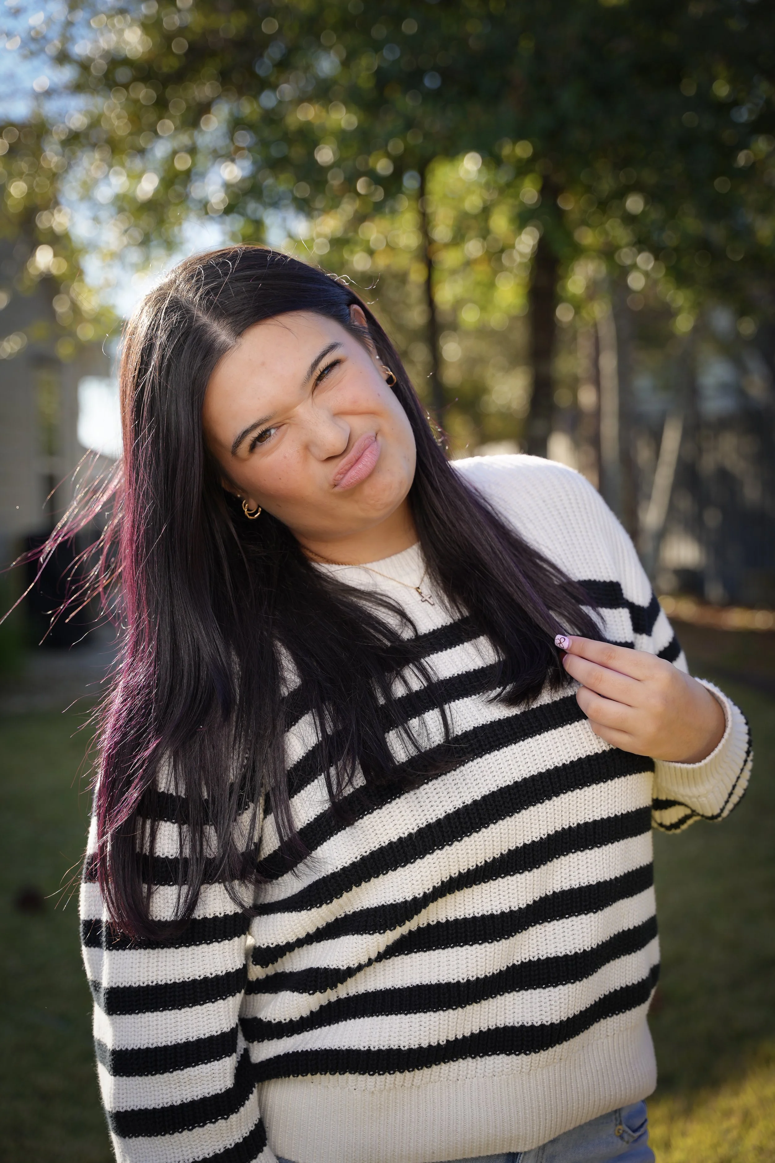Teenage girl in a striped sweater laughing among backlit autumn trees, portrait session in Fort Mill SC
