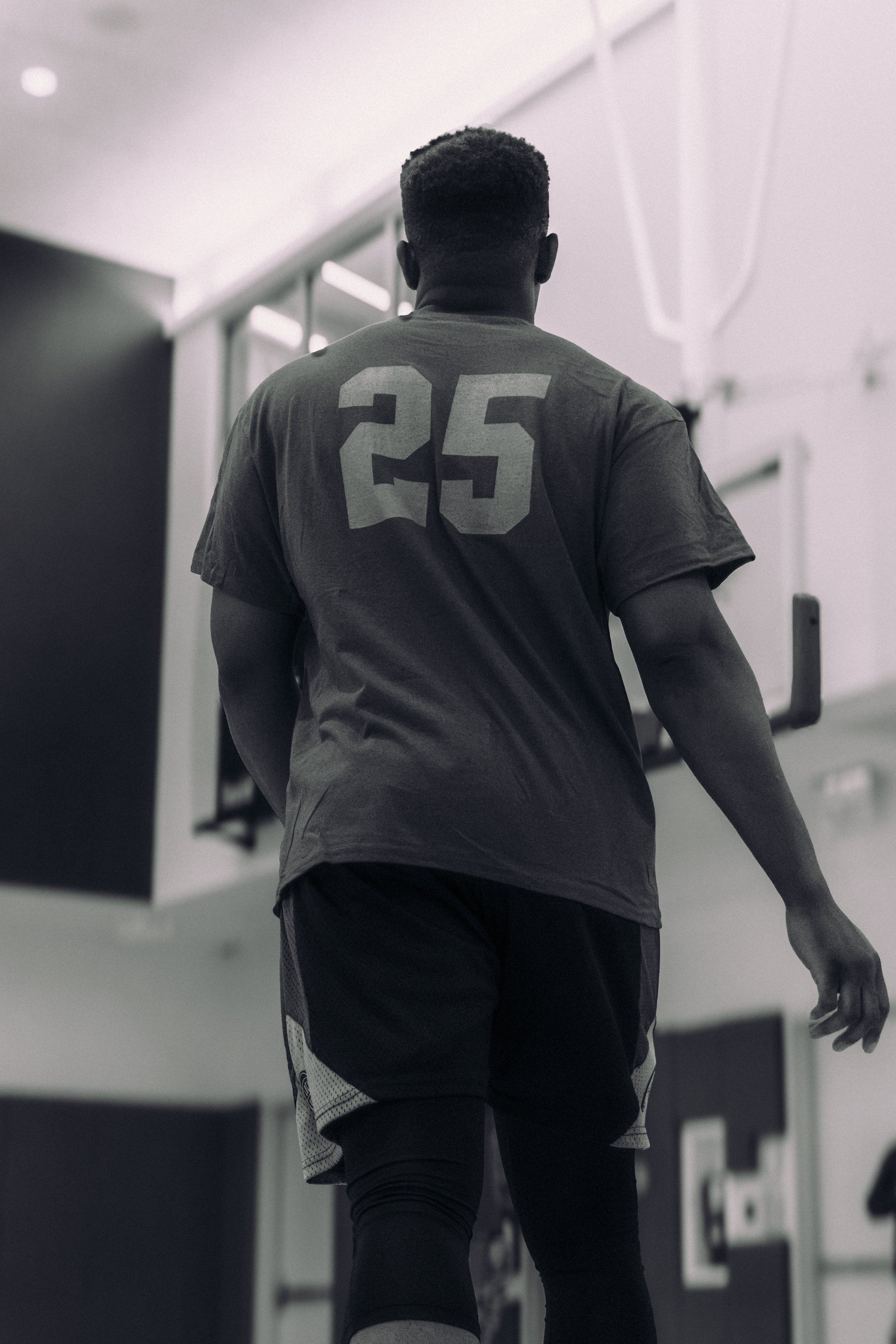Ein männlicher Athlet trägt ein graues Sportshirt mit der Nummer 25 auf dem Rücken, während er in einem Fitnessstudio trainiert.