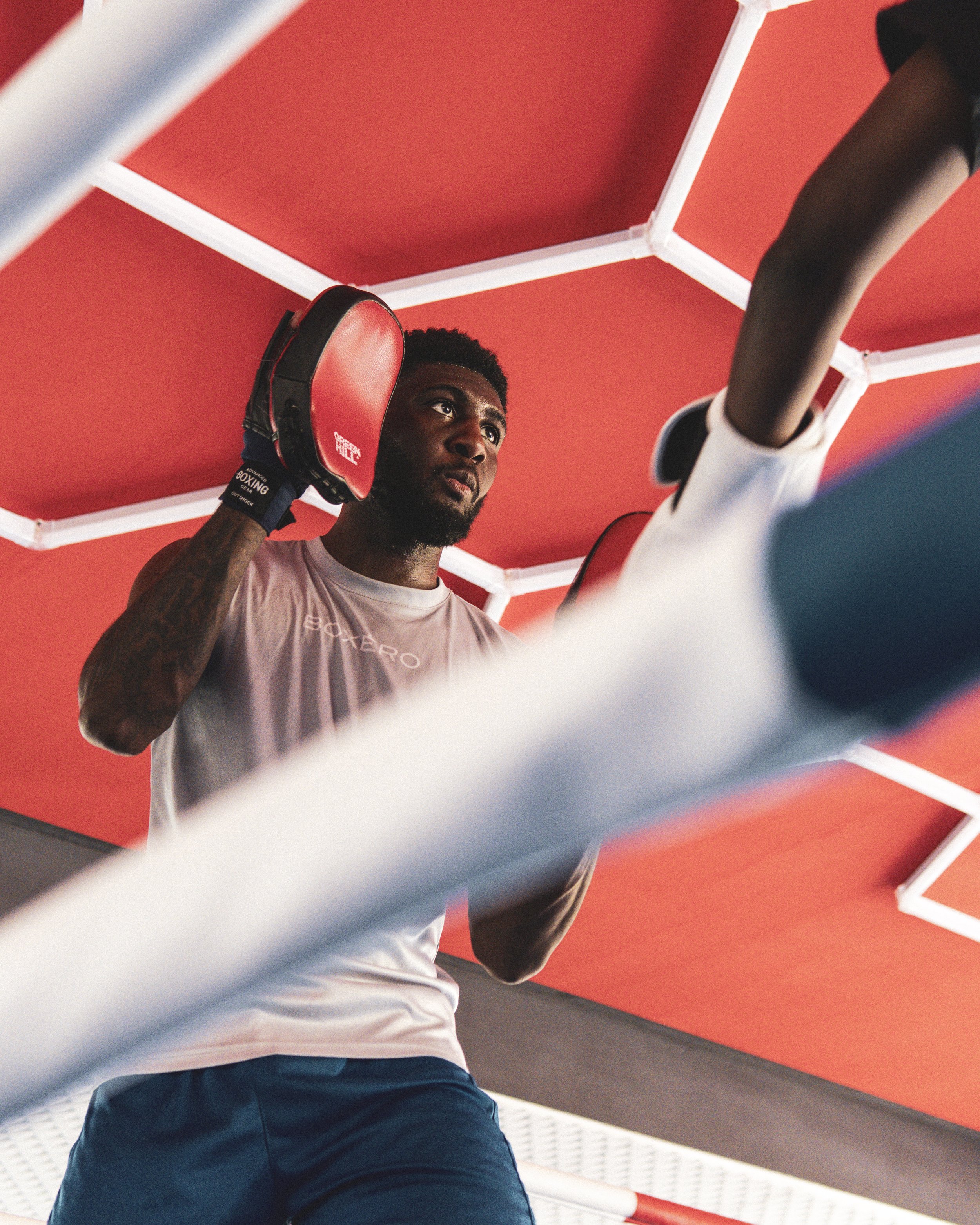 Ein männlicher Boxer trägt rote PRÜGELHANDSCHUHE und bereitet sich auf einen Kampf vor, während er in einem Boxstudio steht, mit roter Wand im Hintergrund.