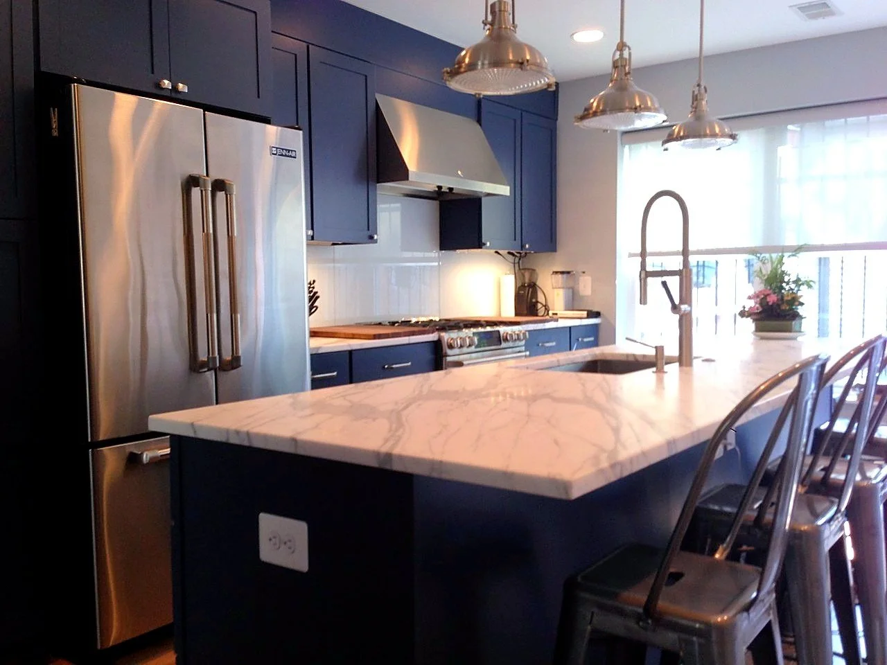 Navy kitchen with a marble island, brass pendant lights and custom panelled refrigerator