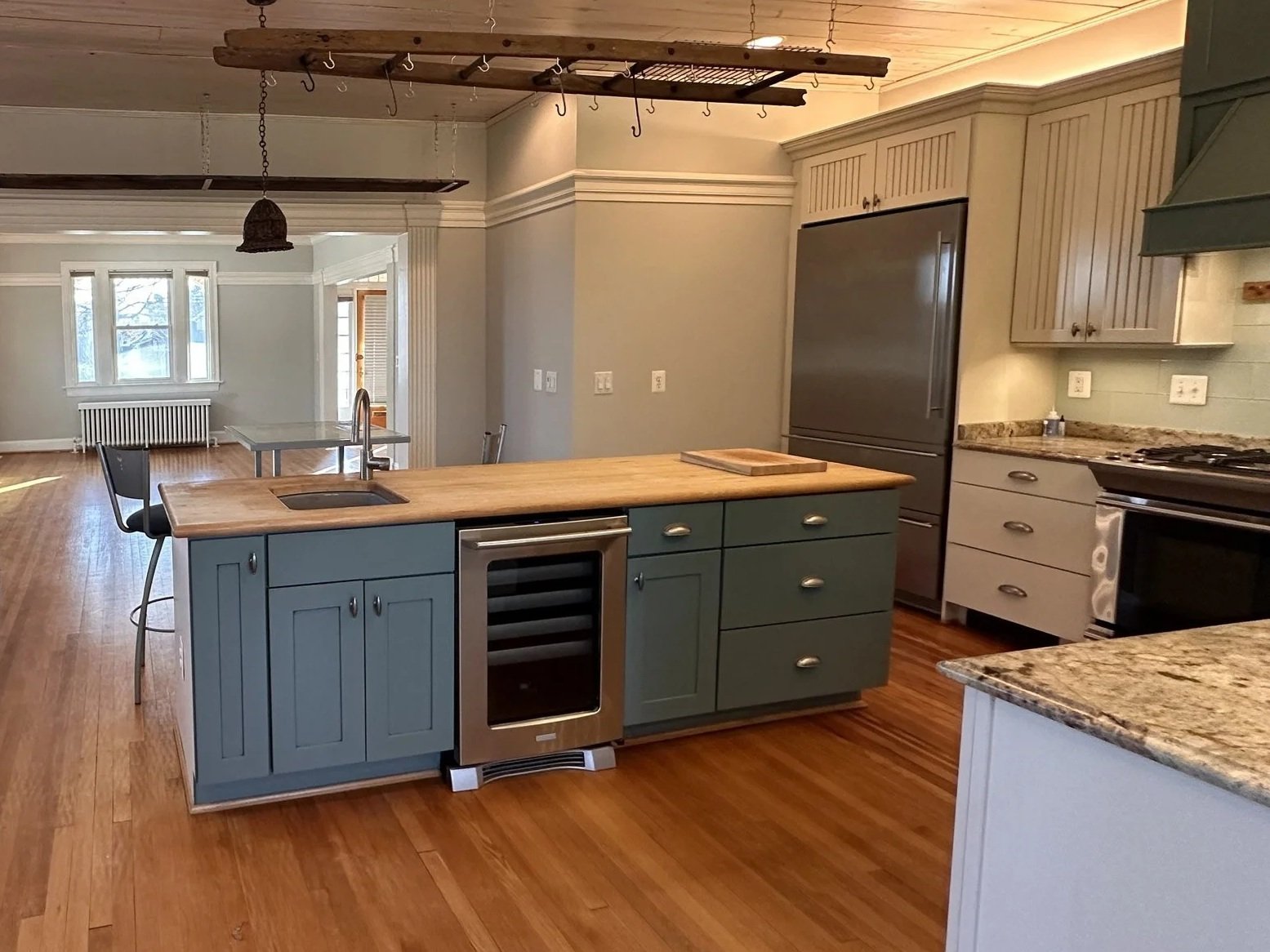 Cream wall cabinets above a teal island base with a butcher-block counter and hanging pot rack