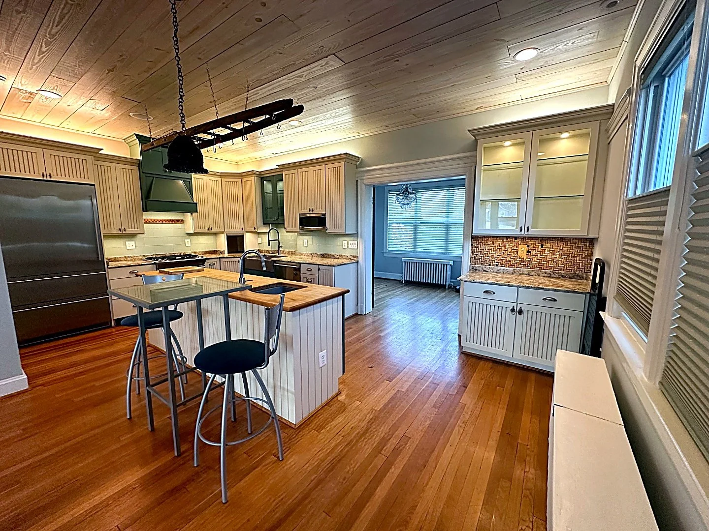 Cream kitchen with a butcher-block island, hanging pot rack and pine plank ceiling
