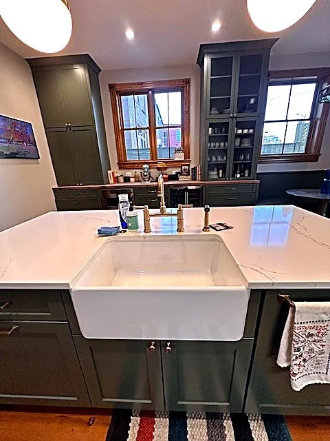 Dark green island with a white farmhouse apron sink and granite countertop