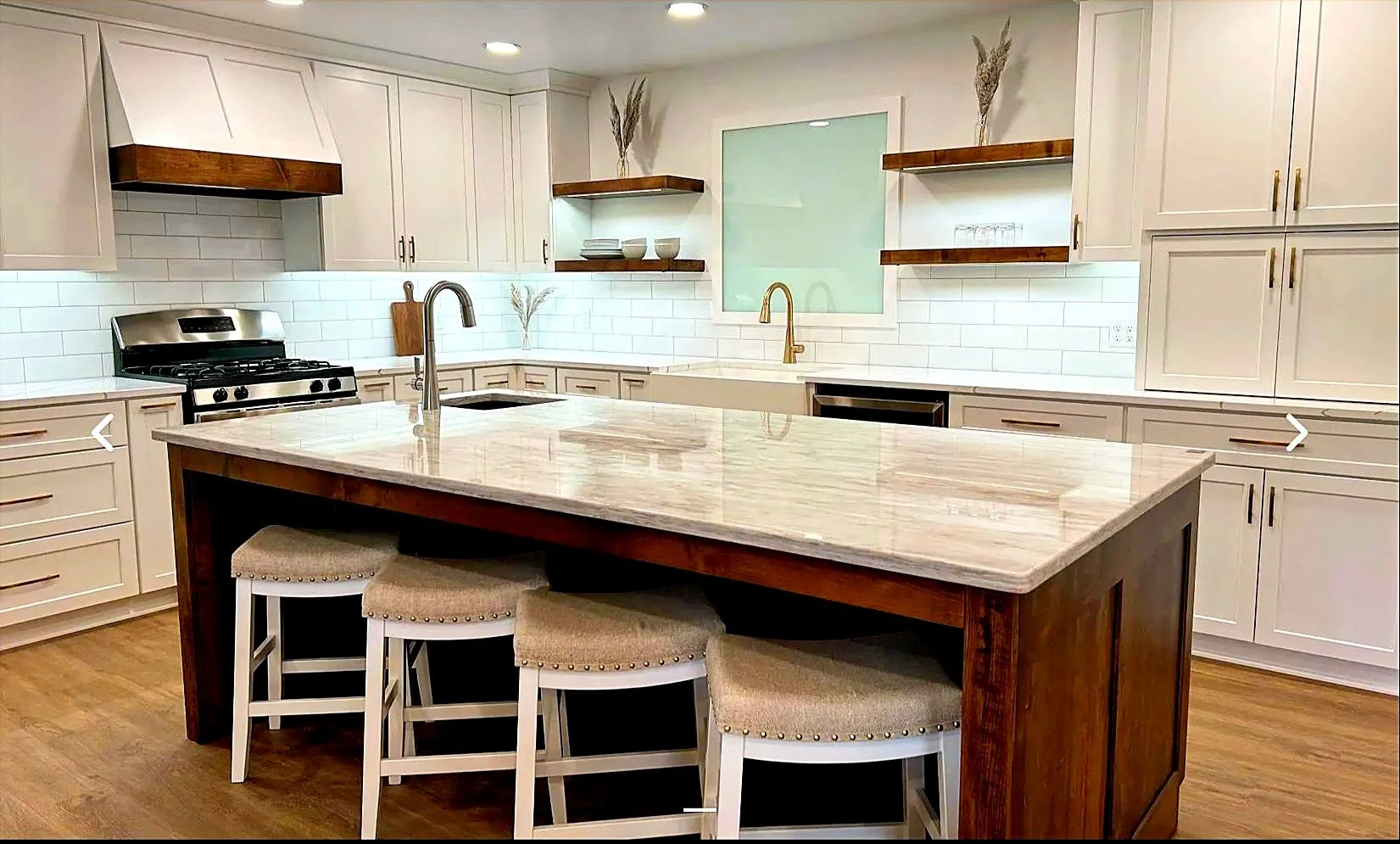 White kitchen with a granite island, walnut open shelving and four slipcovered bar stools