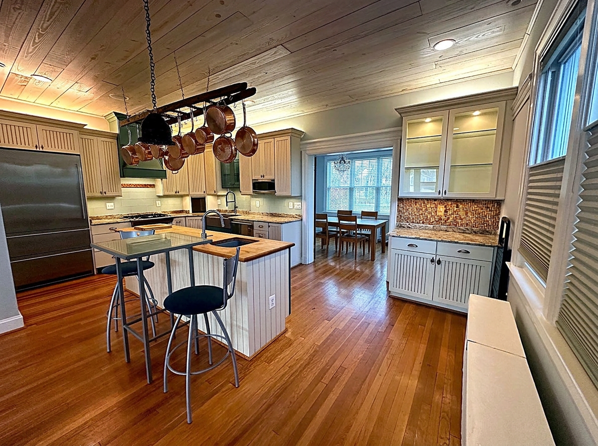 Cream kitchen with a butcher-block island, hanging copper pot rack and pine plank ceiling