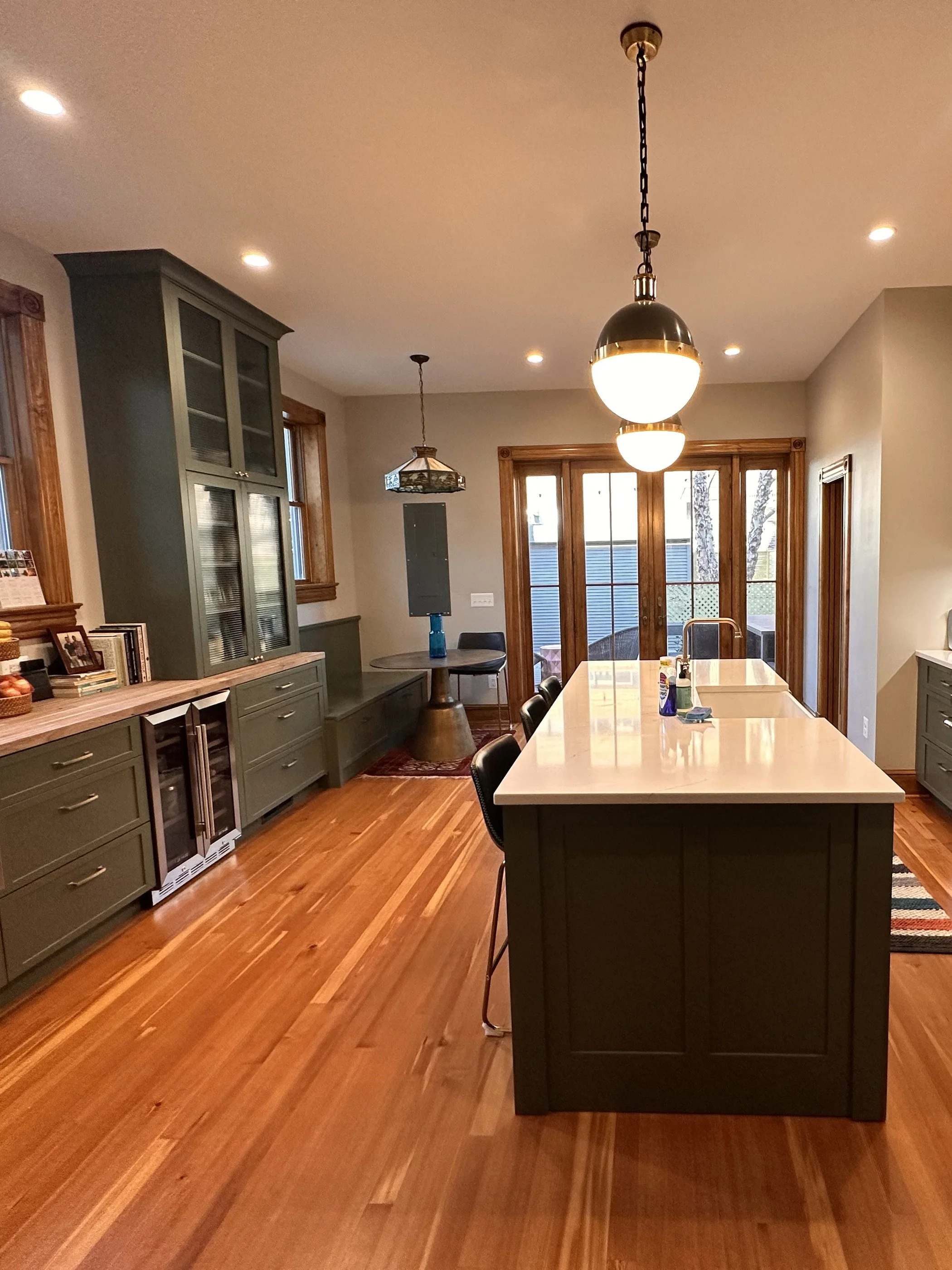 Olive-green kitchen with a long island, glass-front cabinets and pendant lights over cherry floors