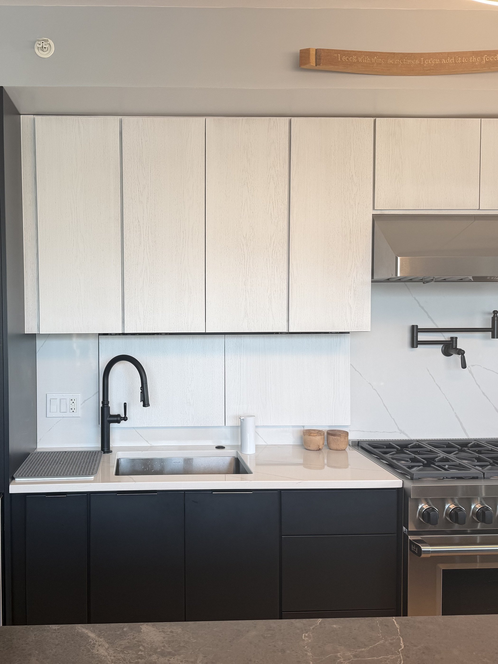Matte black base cabinets with white oak uppers, a stone counter and professional range