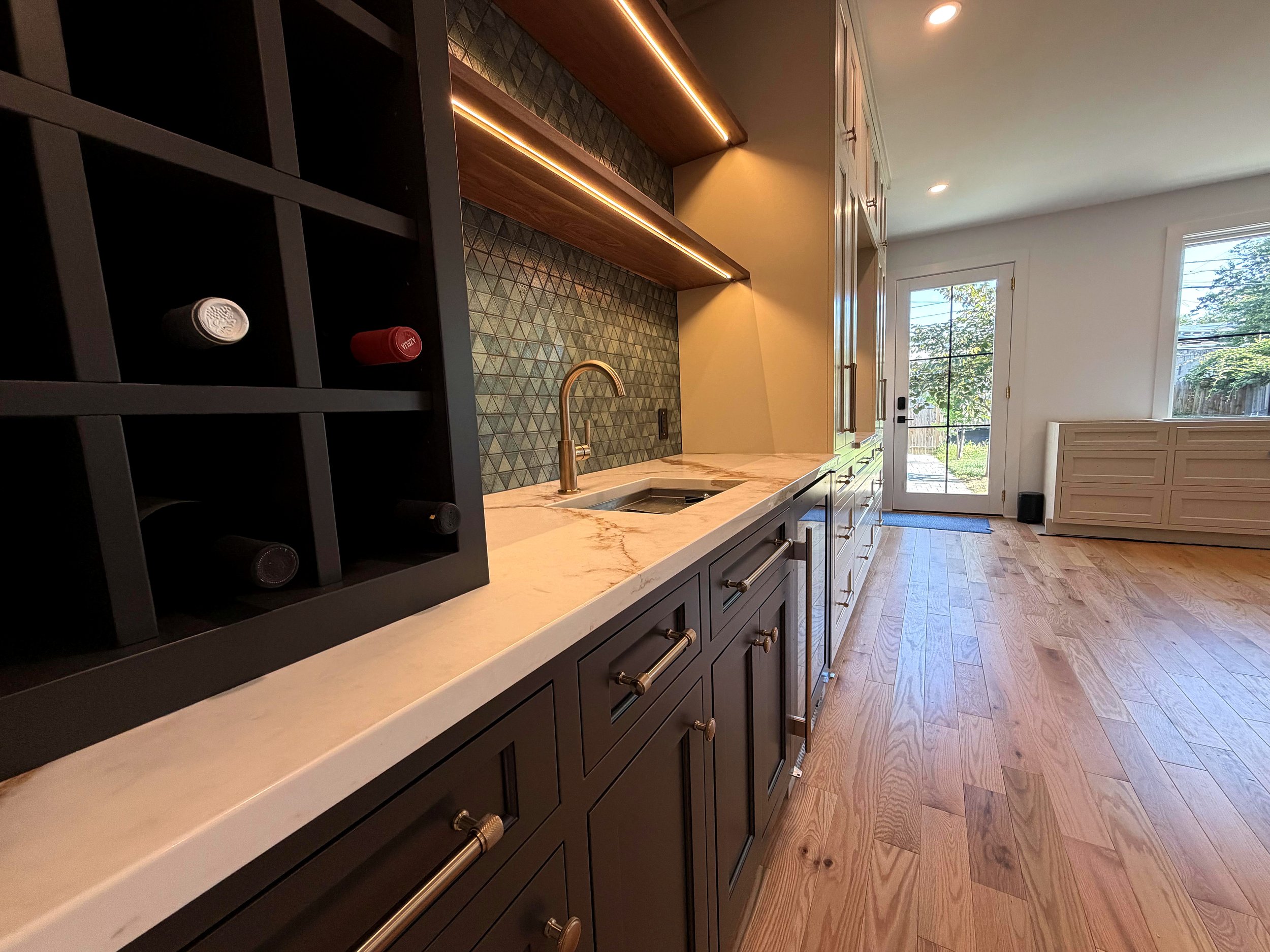 Walnut base cabinets with a quartz countertop, green tile backsplash and brass faucet