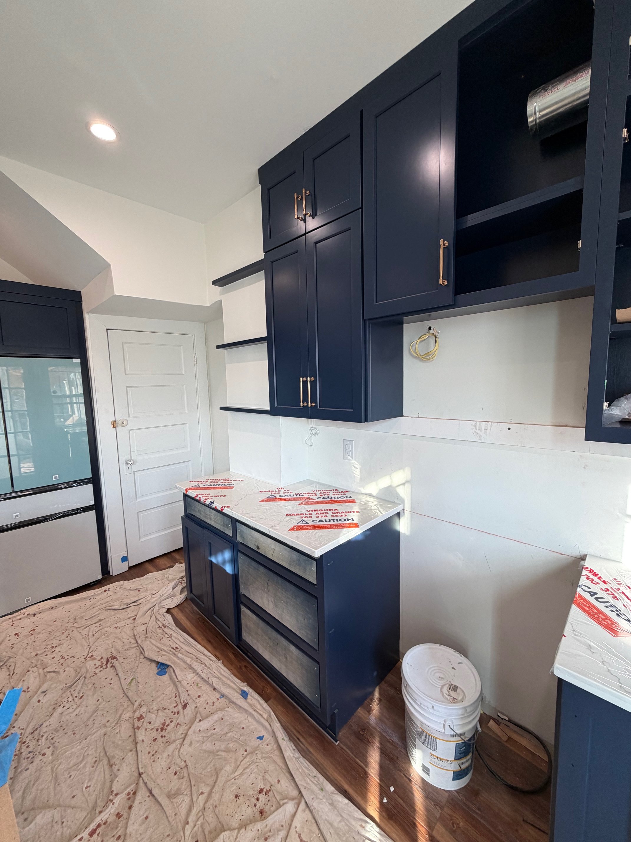Navy kitchen cabinets being installed, with the island and upper runs already set in place