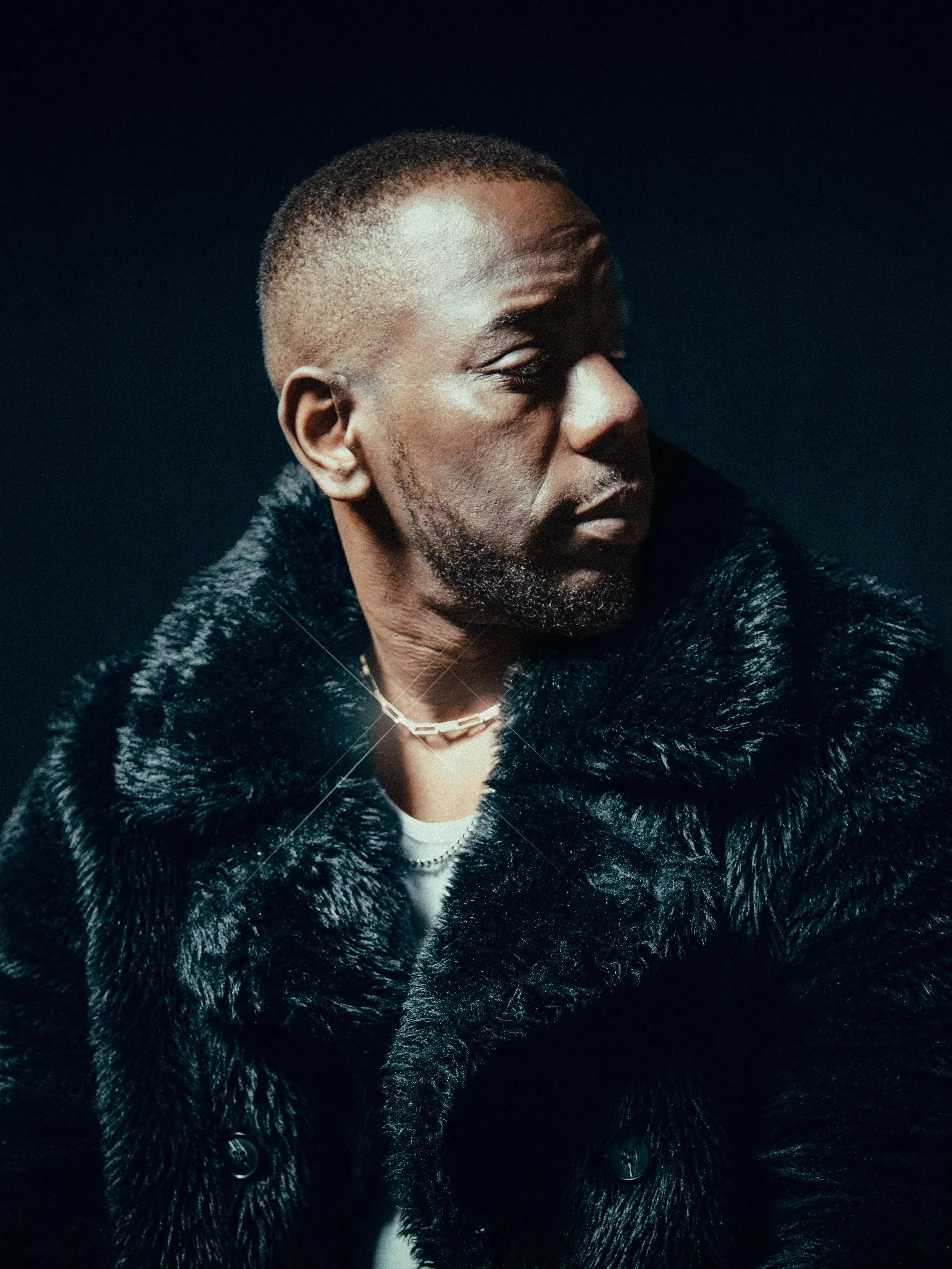 Portrait of Double S in a fur coloured coat styled in a moody editorial press shoot with dramatic side lighting