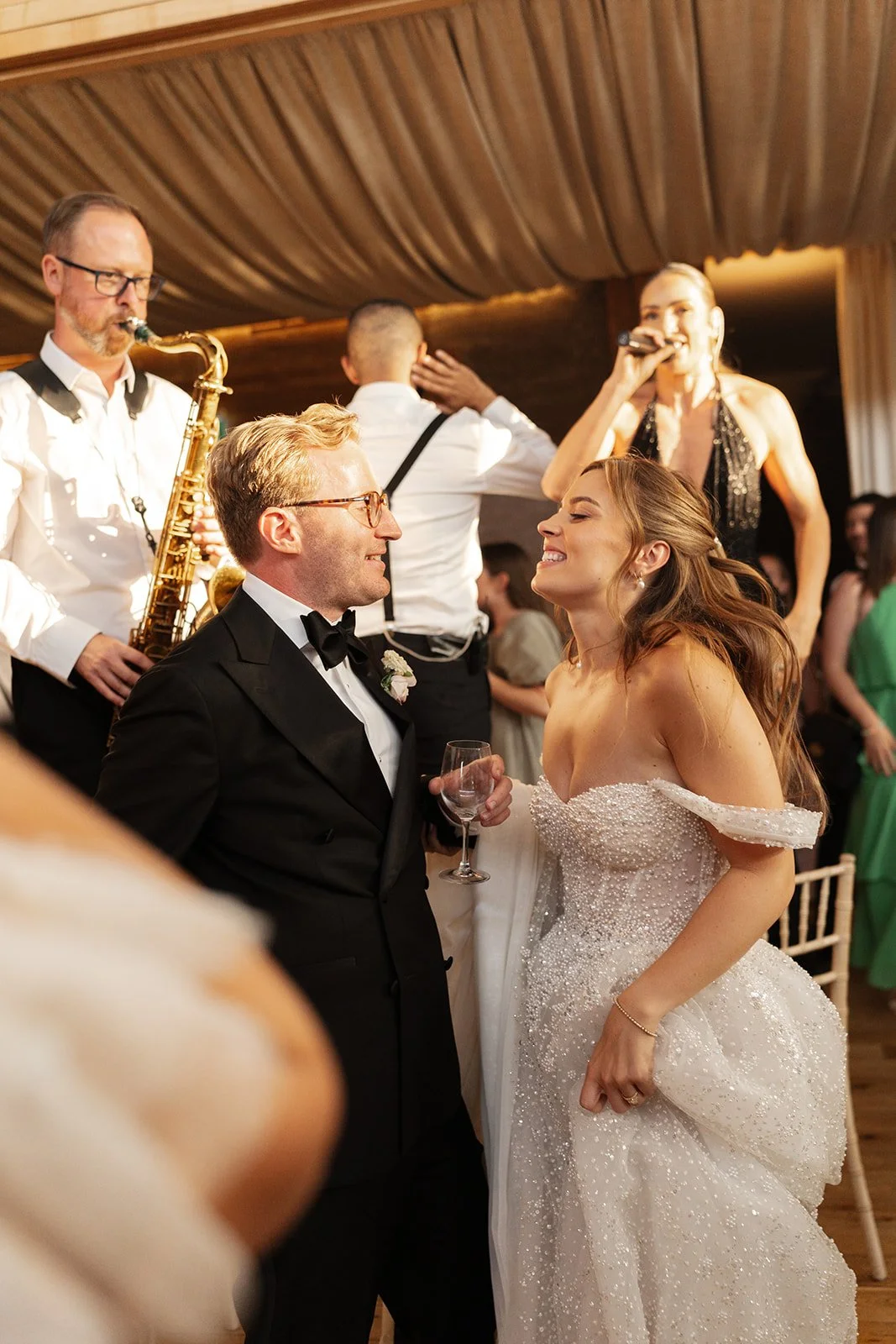 Bride and groom smiling at each other during a wedding reception with a band playing in the background.