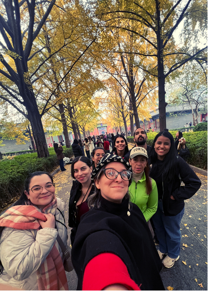 Grupo de personas sonriendo en un parque con árboles de hojas amarillas y caminos asfaltados.