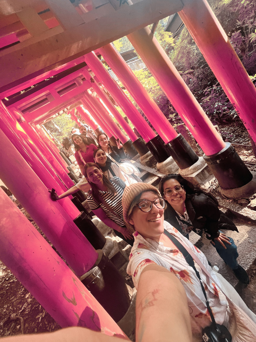 Grupo de personas tomando una selfie en fila en un camino entre puertas torii rosadas en un santuario, rodeados de naturaleza.