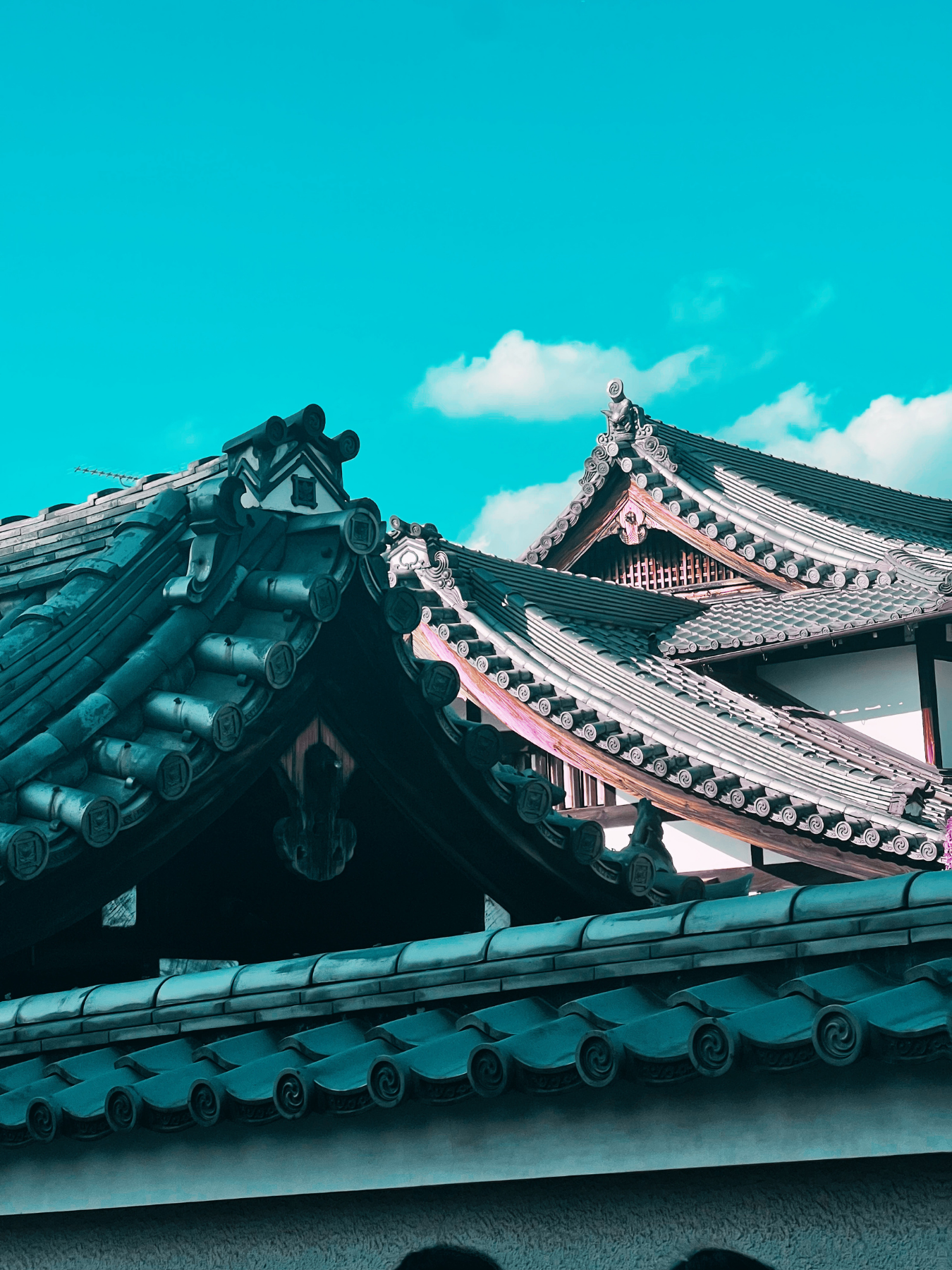 Techo de estilo tradicional japonés con tejas curvas y decorativas bajo un cielo azul con algunas nubes.