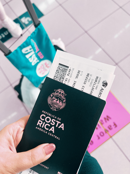 Pasaporte de Costa Rica con itinerario de vuelo y tarjeta de embarque en mano, en aeropuerto.
