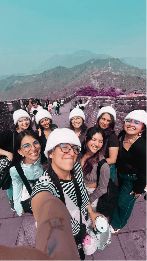 Grupo de turistas en la Muralla China, todos llevan gorros blancos y sonríen para la selfie.