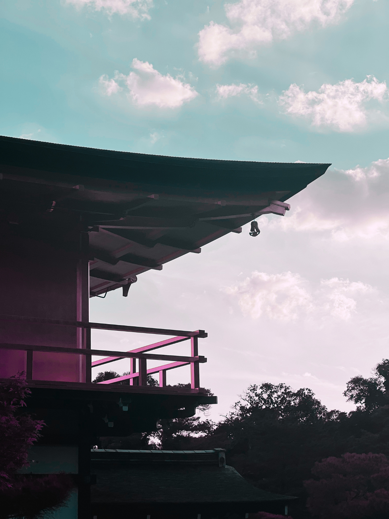 Edificio con balcón y estructura en color rosa, con cielo despejado y algunas nubes, árboles en el fondo.
