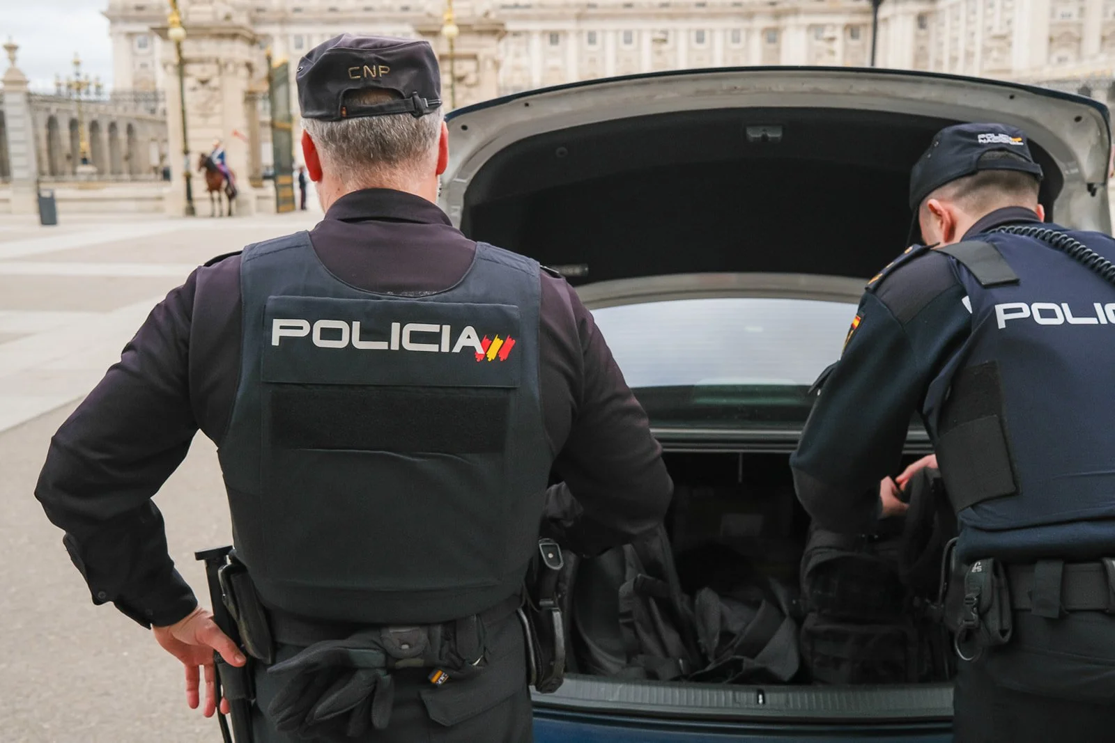 Two police officers in uniform inspecting the trunk of a vehicle in an urban area.