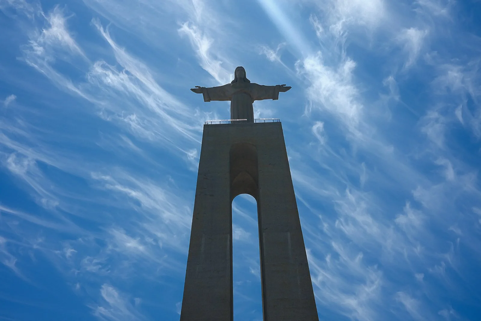 The Christ the Redeemer statue against a bright blue sky with wispy clouds.
