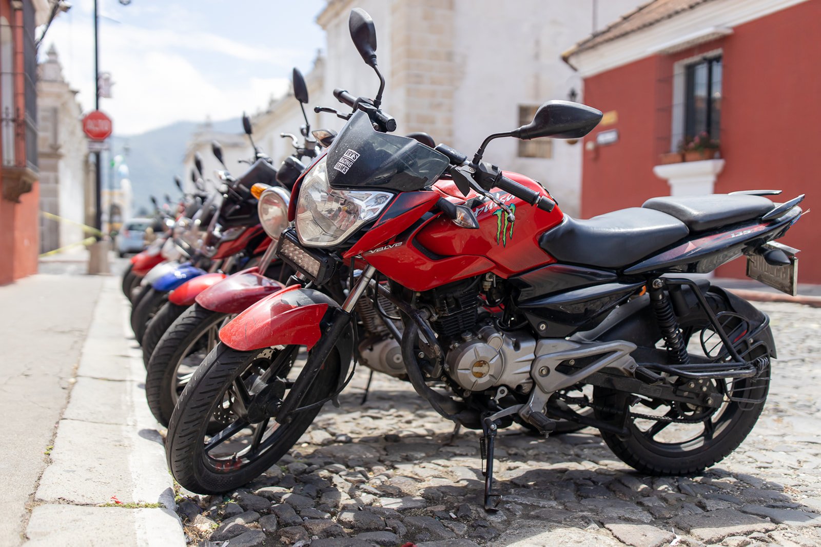 Several motorcycles parked along a cobblestone street in front of buildings with colorful facades.