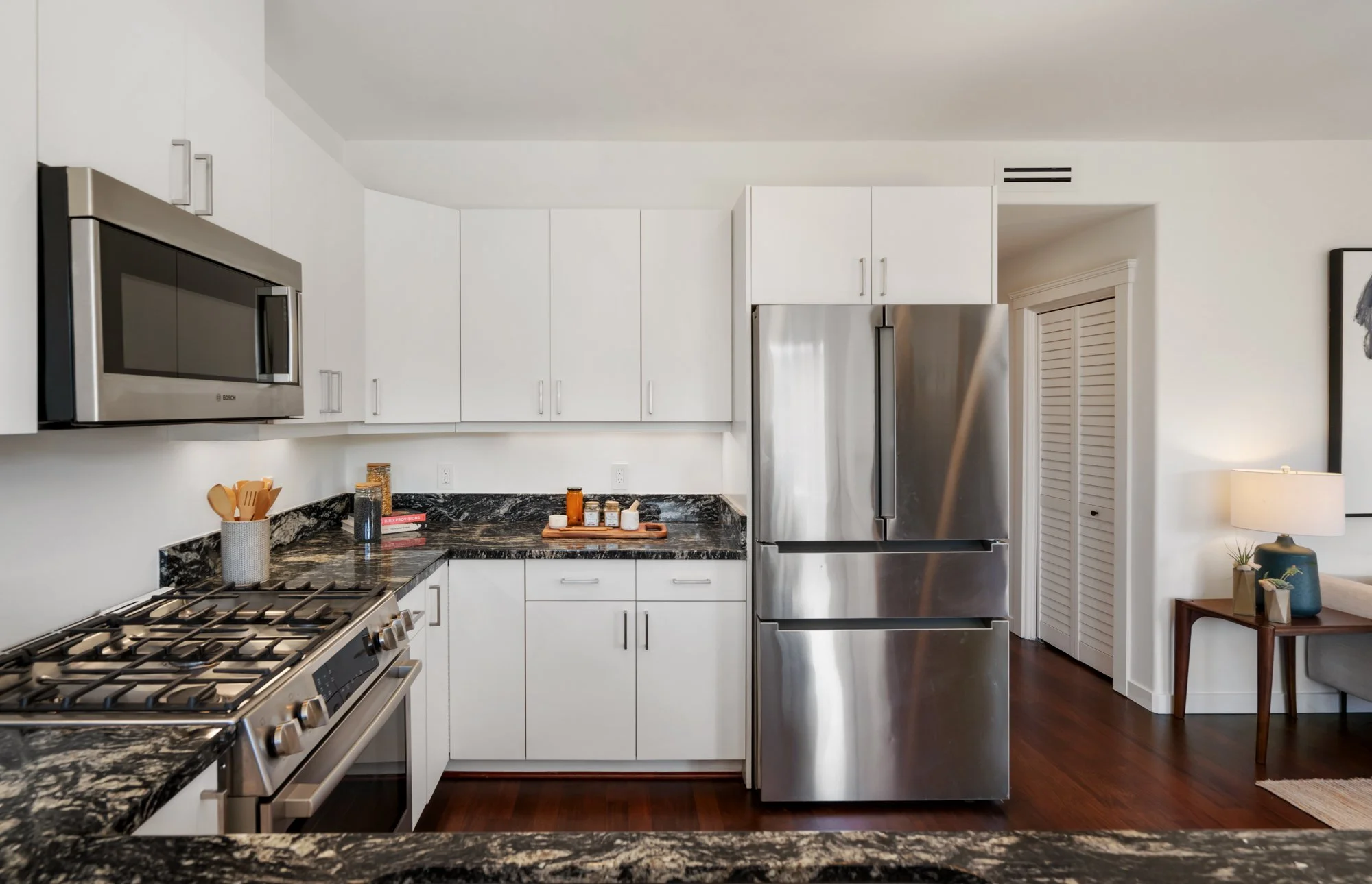 Modern kitchen with white cabinets, stainless steel appliances, black granite countertops, and dark wood flooring.