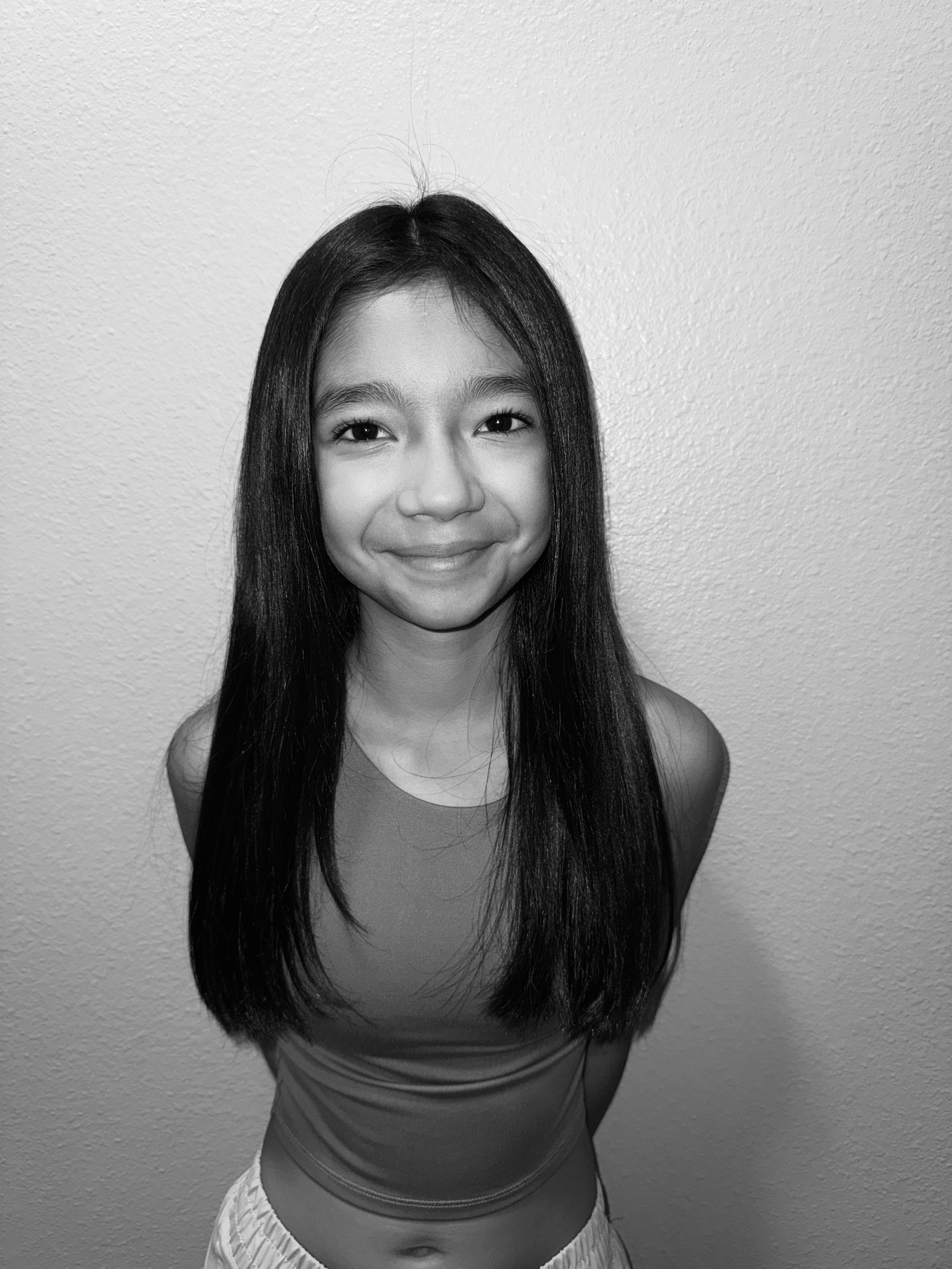 A young girl with long, straight hair smiling in front of a textured wall.