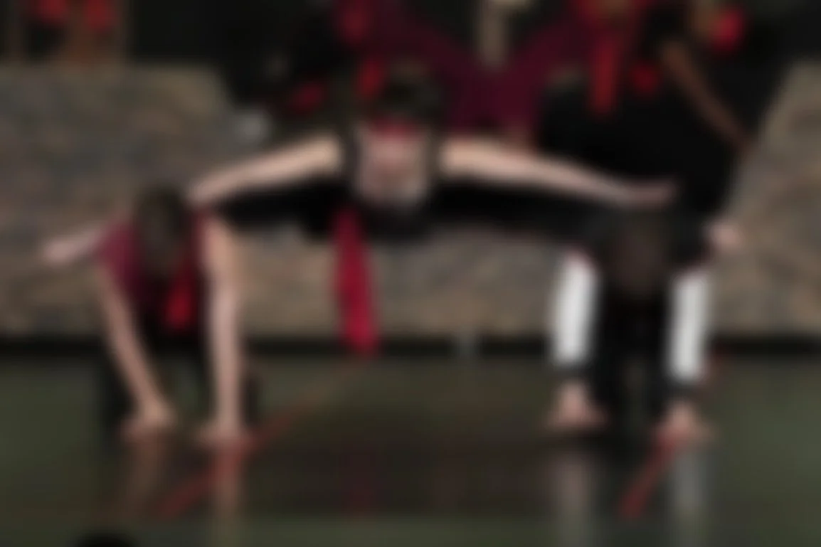 Two people practicing acro yoga on a mat in a gym, with a woman performing a handstand supported by a man lying on his back.