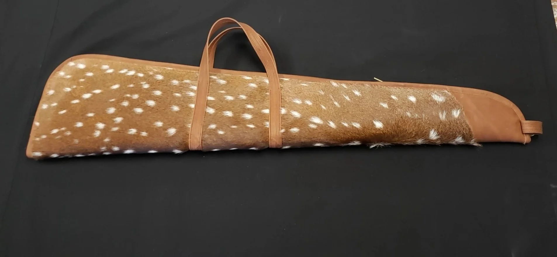 A rolled-up deer hide with white spots and brown leather edges, placed on a black surface.