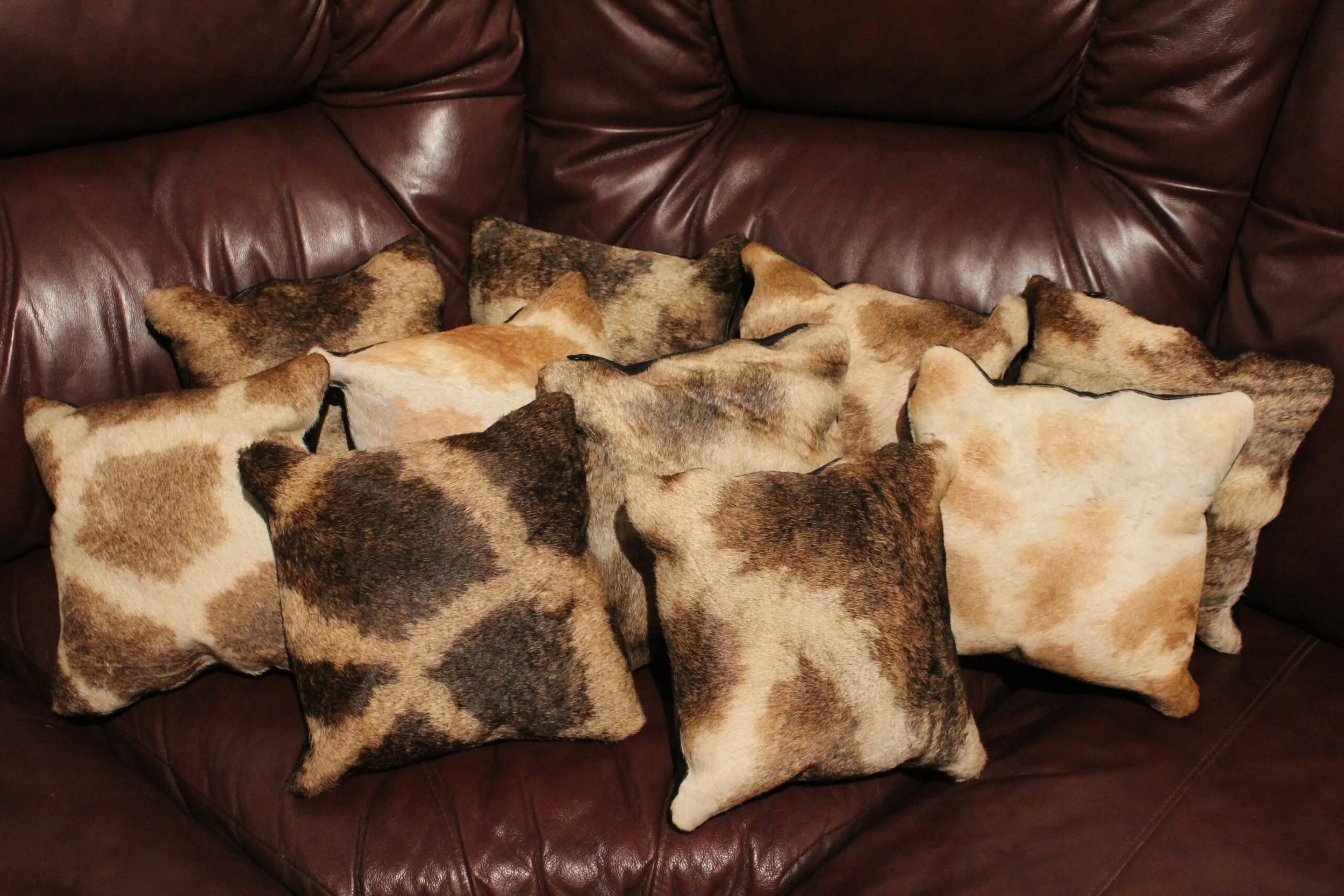 Several giraffe pillows arranged on a dark brown leather couch. 