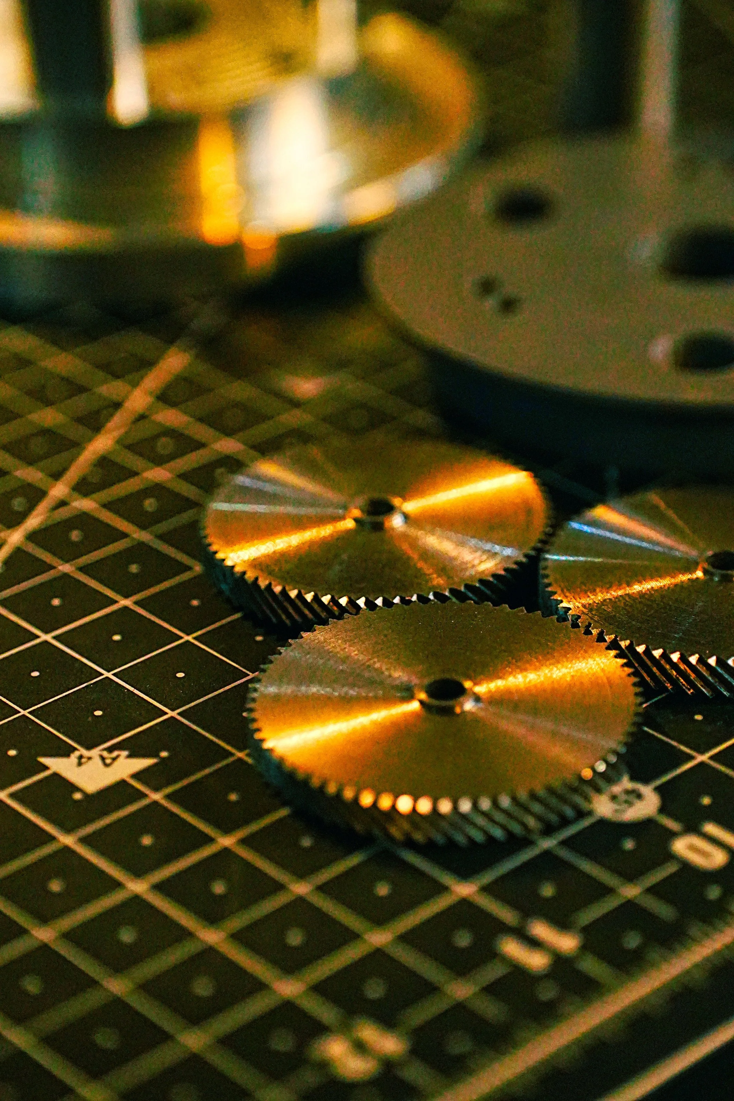 Close-up of gold-colored circular saw blades with sharp teeth, placed on a black cutting mat with a grid pattern.