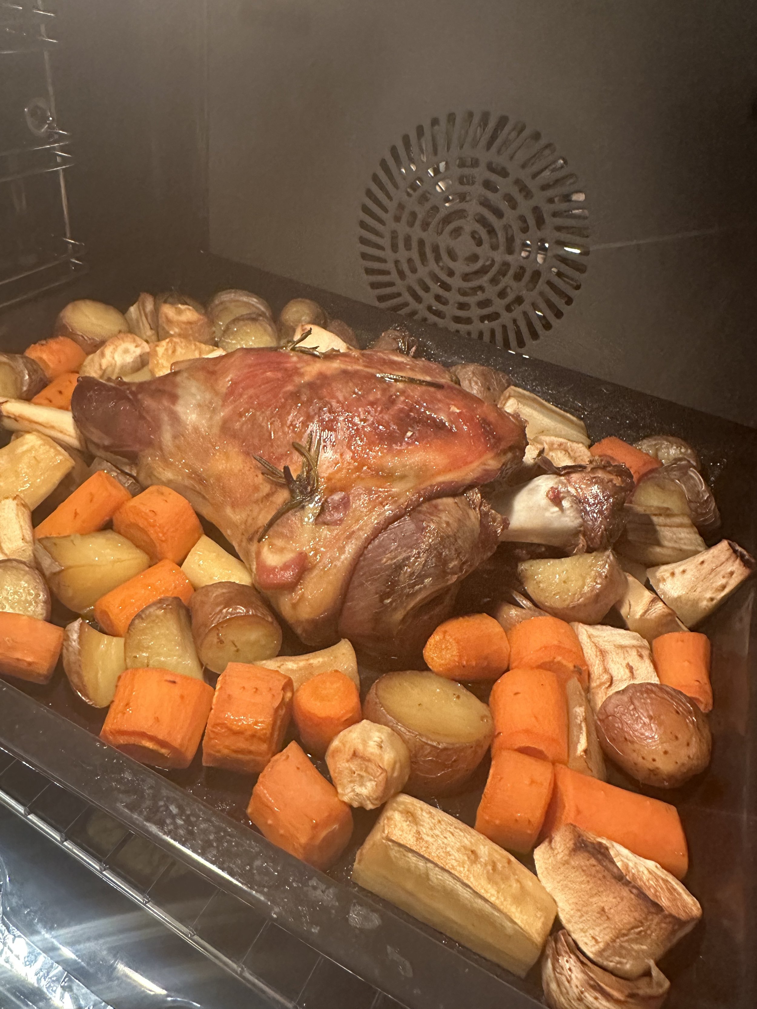 Roast chicken with roasted potatoes, carrots, and garlic, inside an oven.