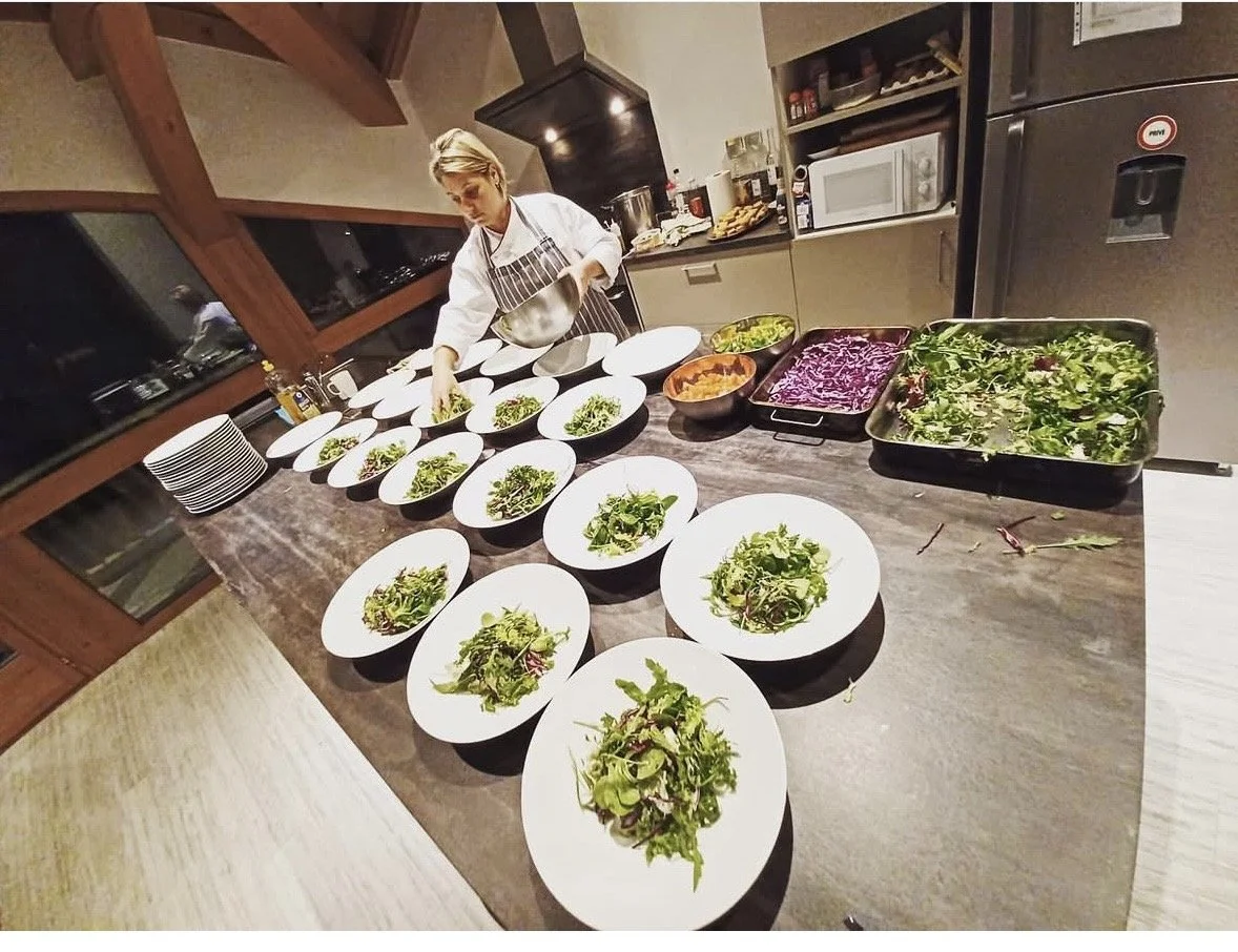 A woman preparing multiple bowls of salad on a kitchen countertop with various vegetables and greens.