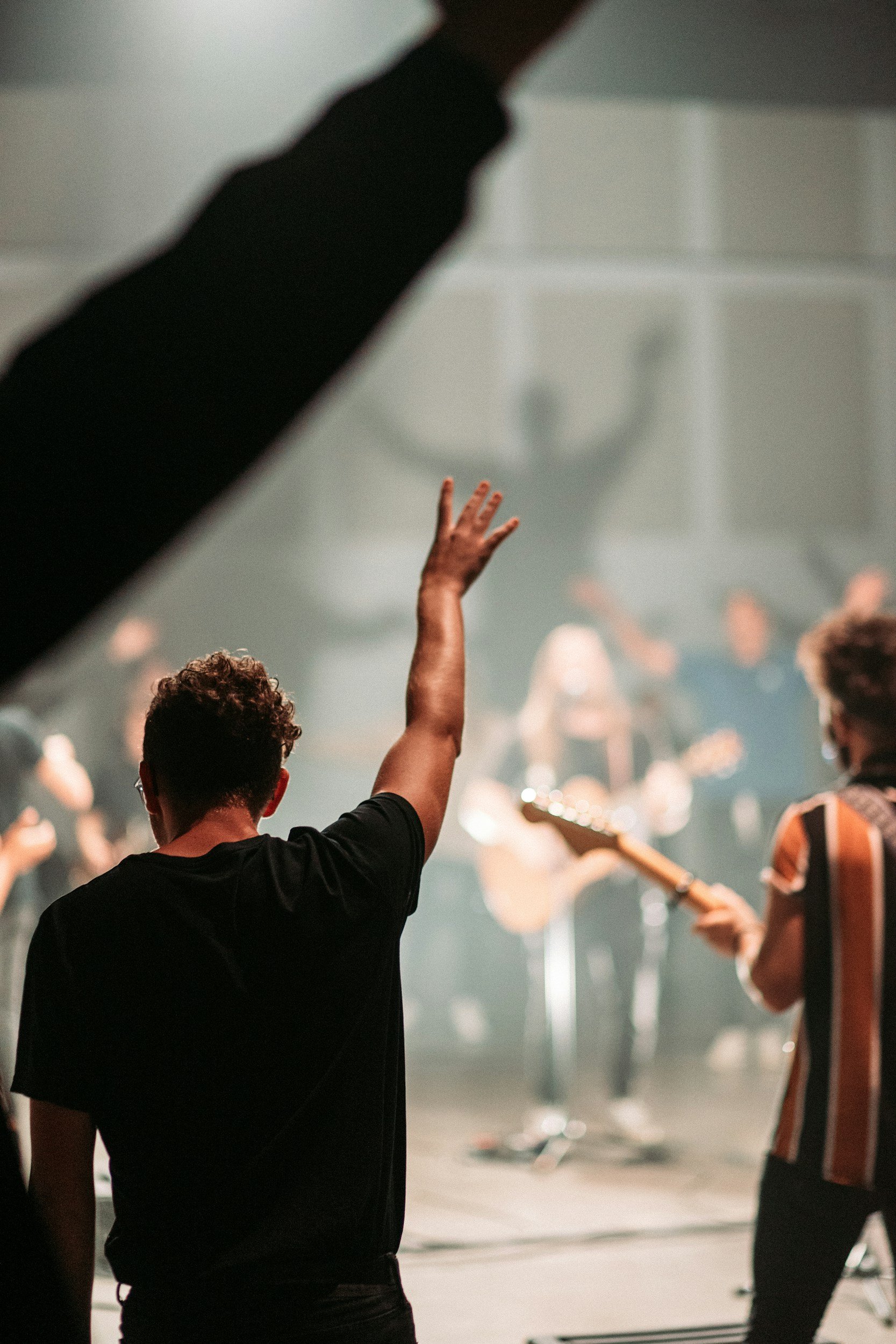 People on stage at a concert or performance, with one person raising their hand and others playing instruments.