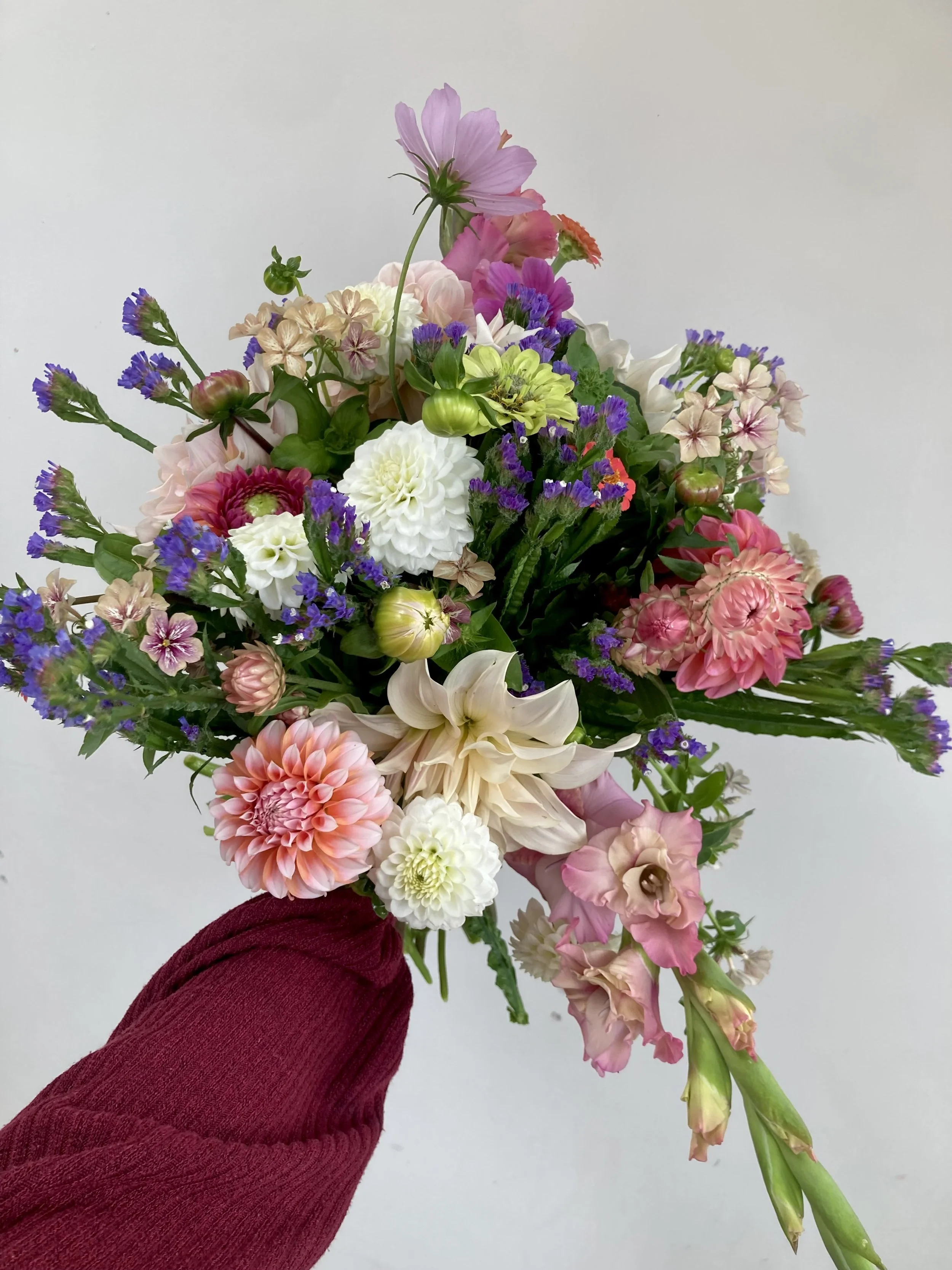 A person wearing a red sweater holding a large bouquet of mixed colorful flowers against a plain white background.