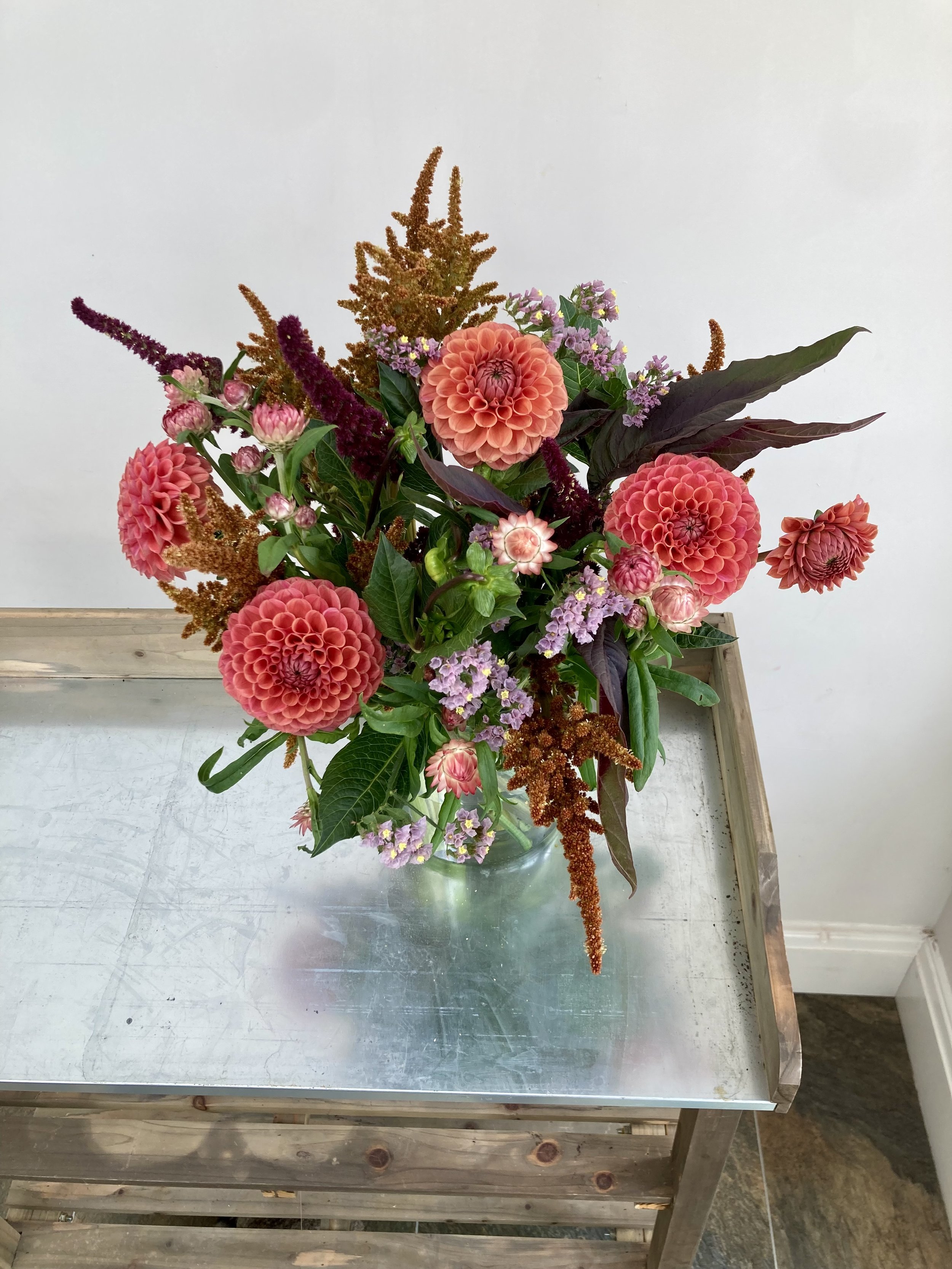 A colorful floral arrangement in a glass vase on a metallic table against a plain white background.