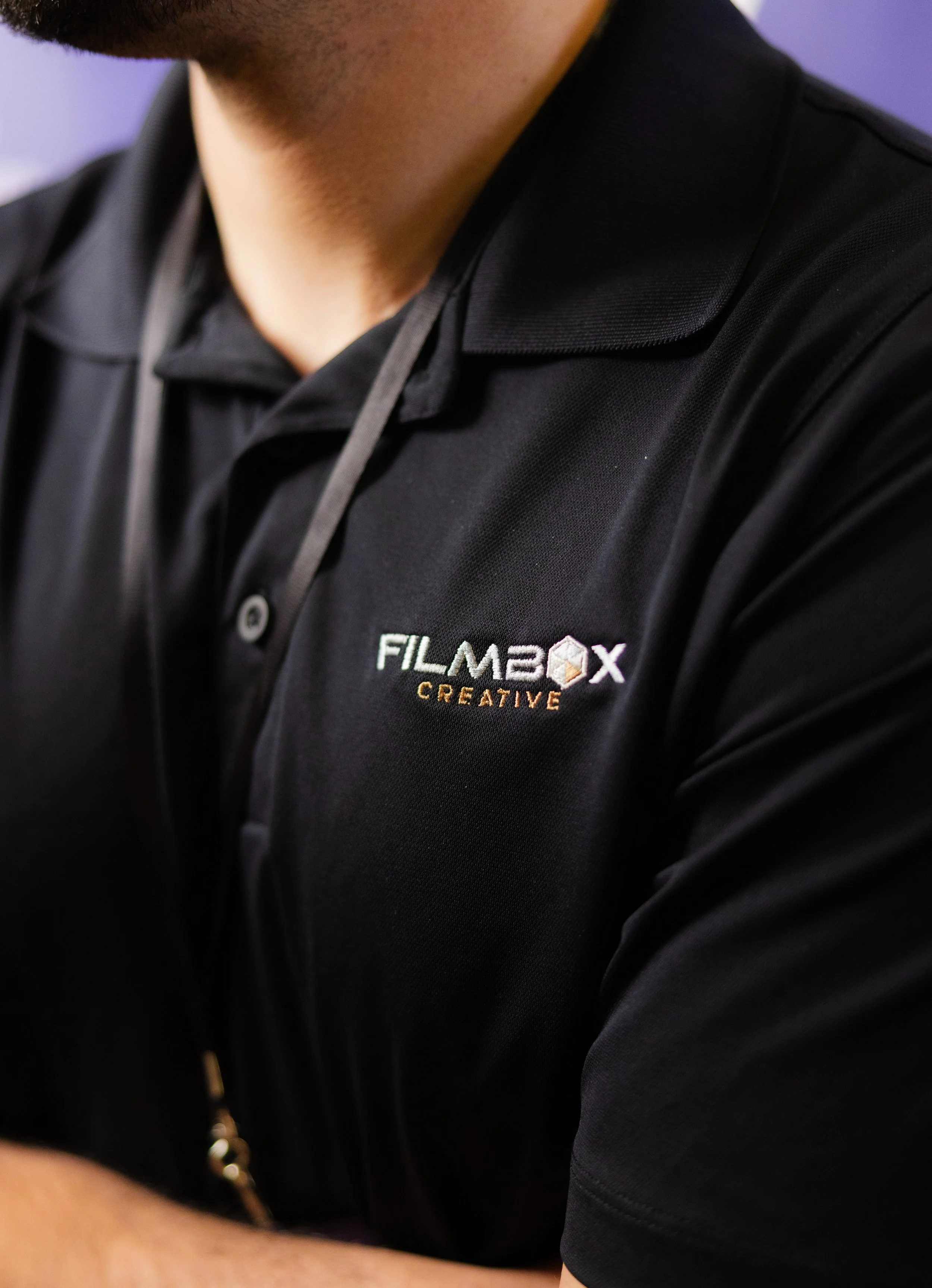 Close-up of a person wearing a black polo shirt with a 'FILMBOX CREATIVE' logo embroidered on it.